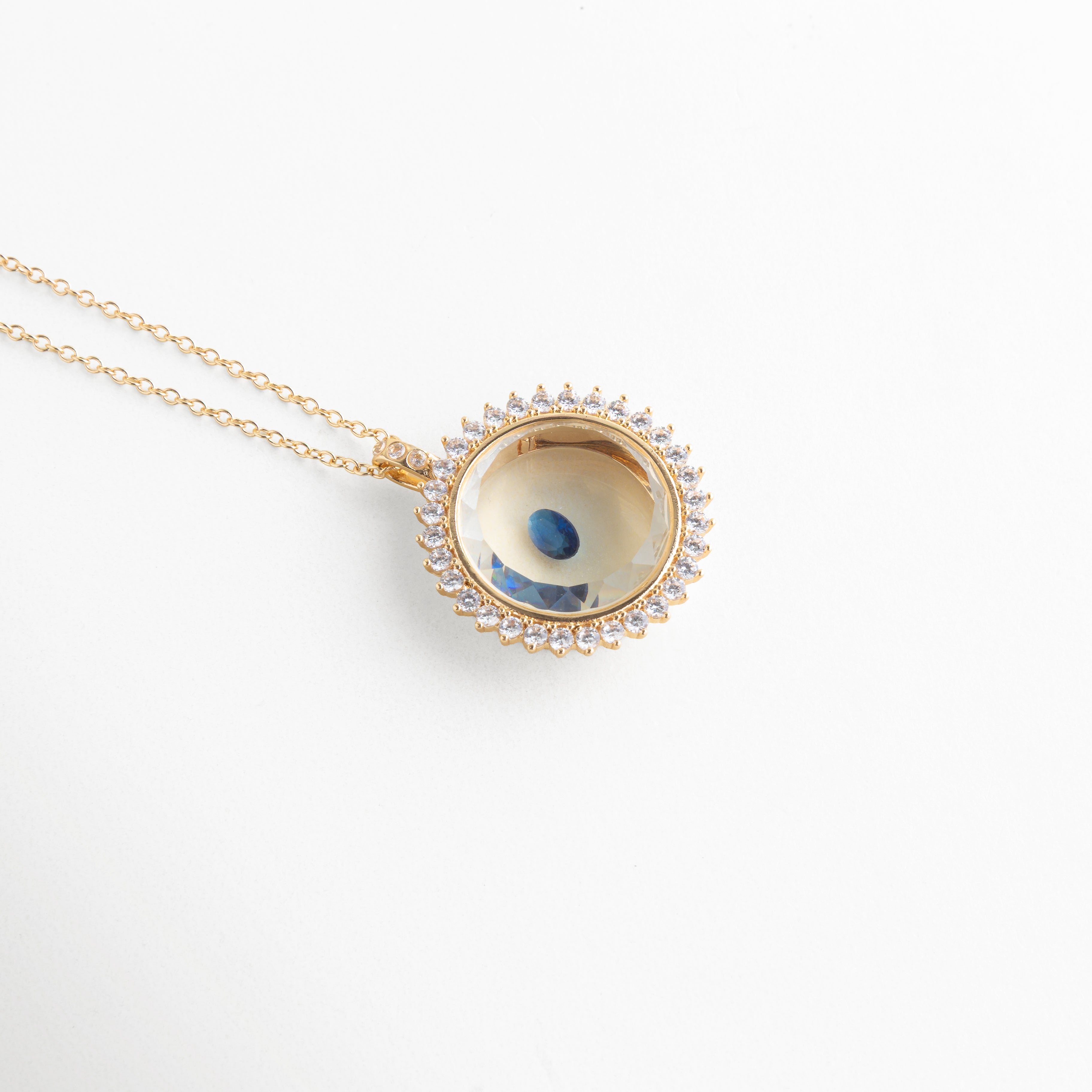 Collar dorado con dije circular y piedra de cristal azul central, Dije elegante con cristal azul brillante en diseño tipo ojo, Joyería fina con piedra azul de cristal en accesorio minimalista, Collar delicado con cristal azul pequeño en acabado brillante, Accesorio de bisutería con gema azul en diseño moderno y fino
