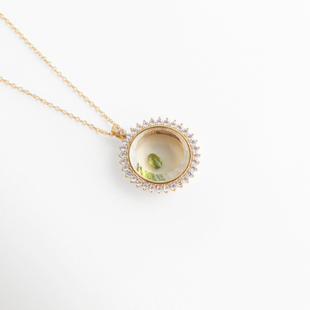 Collar dorado con dije circular y piedra de cristal verde central, Dije elegante con cristal verde brillante en diseño tipo ojo, Joyería fina con piedra verde de cristal en accesorio minimalista, Collar delicado con cristal verde pequeño en acabado brillante, Accesorio de bisutería con gema verde en diseño moderno y fino