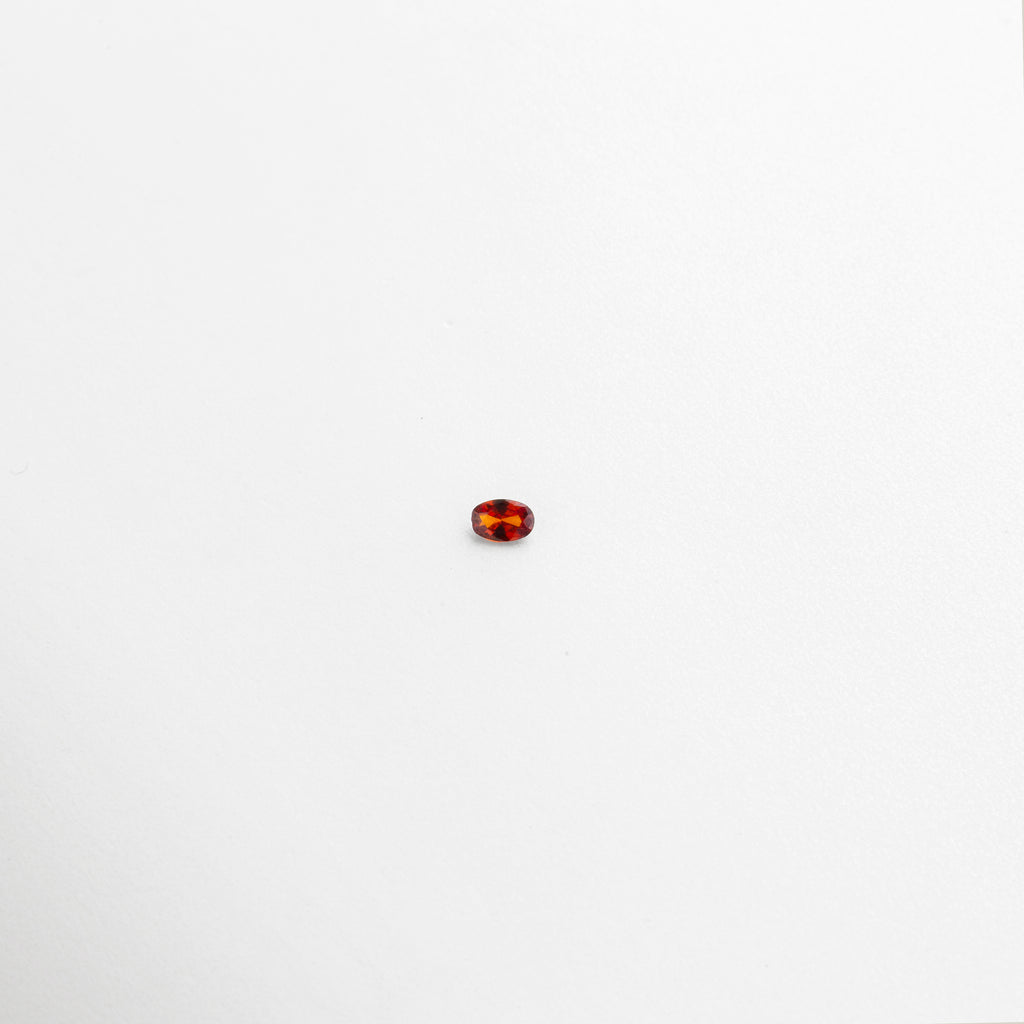 Piedra de cristal ovalada color ámbar con acabado brillante sobre fondo blanco, Cristal decorativo pequeño con tonalidades rojas y naranjas tipo gema, Piedra artificial de cristal en corte ovalado con brillo intenso, Cristal de 0.6 cm color cálido con efecto translúcido y reflejos dorados, Gema de cristal sintético pequeña en tonos ámbar y rojo sobre superficie limpia