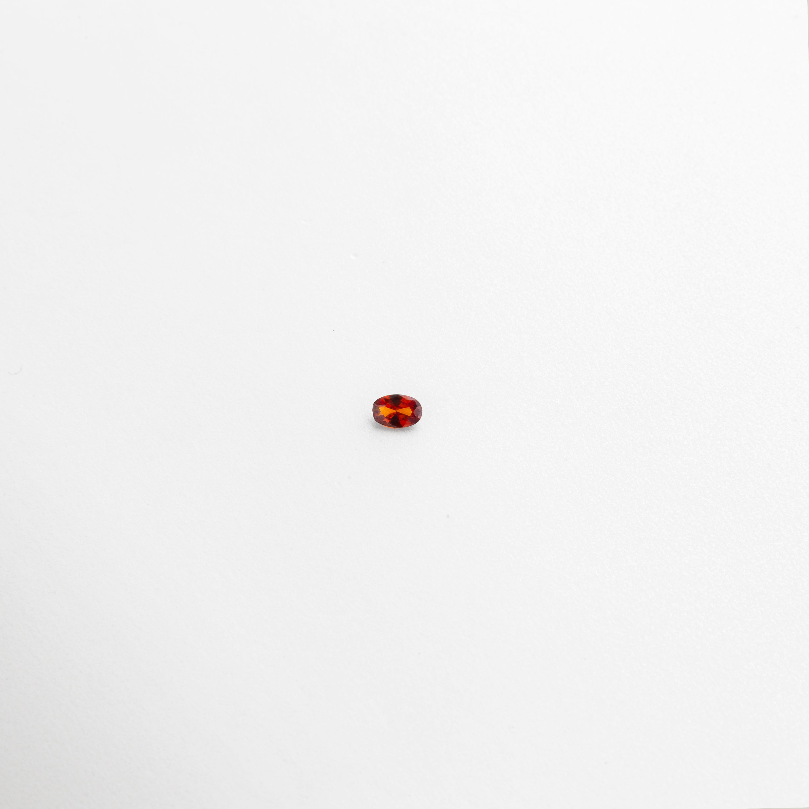 Piedra de cristal ovalada color ámbar con acabado brillante sobre fondo blanco, Cristal decorativo pequeño con tonalidades rojas y naranjas tipo gema, Piedra artificial de cristal en corte ovalado con brillo intenso, Cristal de 0.6 cm color cálido con efecto translúcido y reflejos dorados, Gema de cristal sintético pequeña en tonos ámbar y rojo sobre superficie limpia