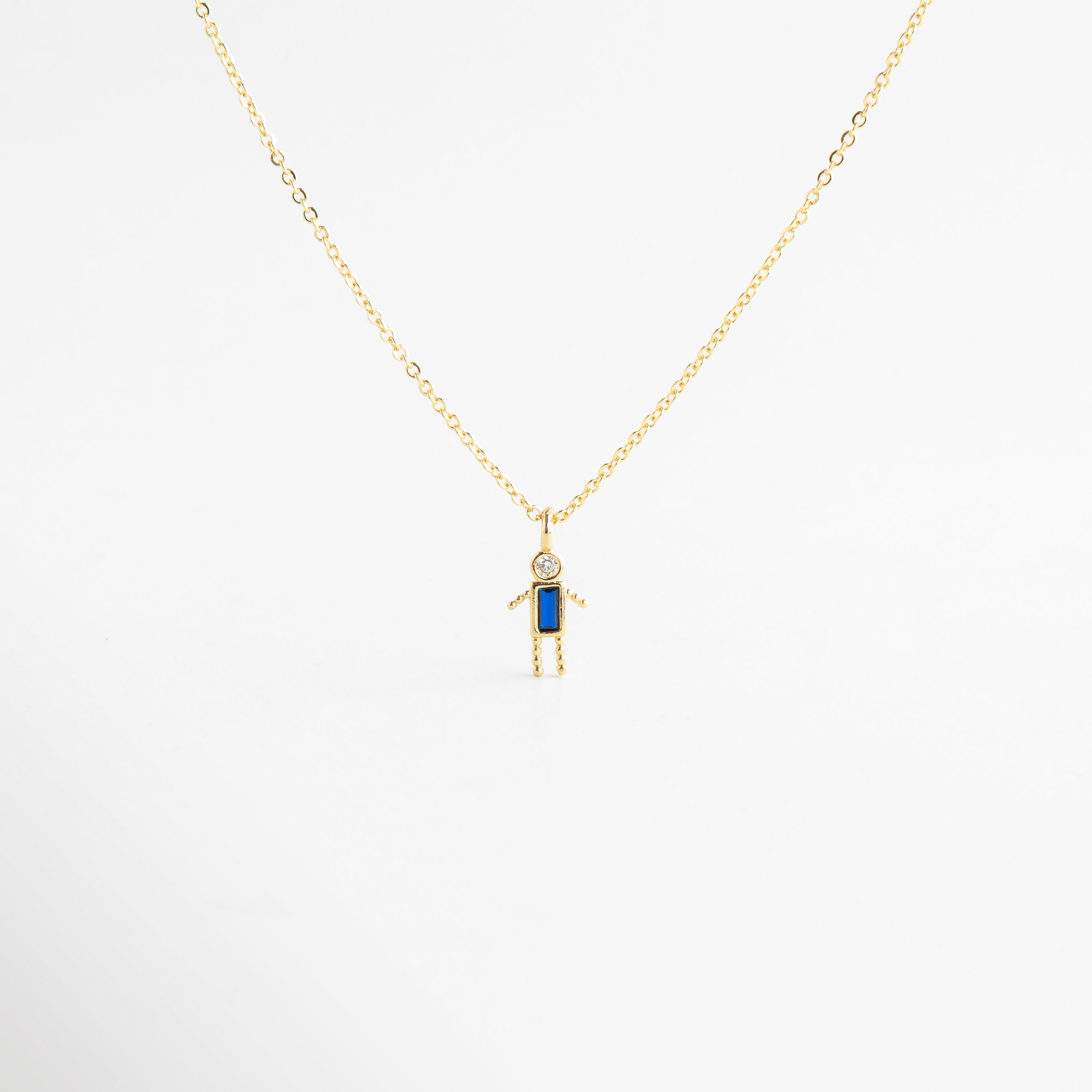 Collar dorado con dije de niño y zirconia azul brillante, Collar delicado con colgante de niño y piedra azul elegante, Collar en oro 18K con dije de niño y zirconia azul, Collar fino dorado con figura de niño y detalle azul, Collar con colgante pequeño de niño y zirconia azul