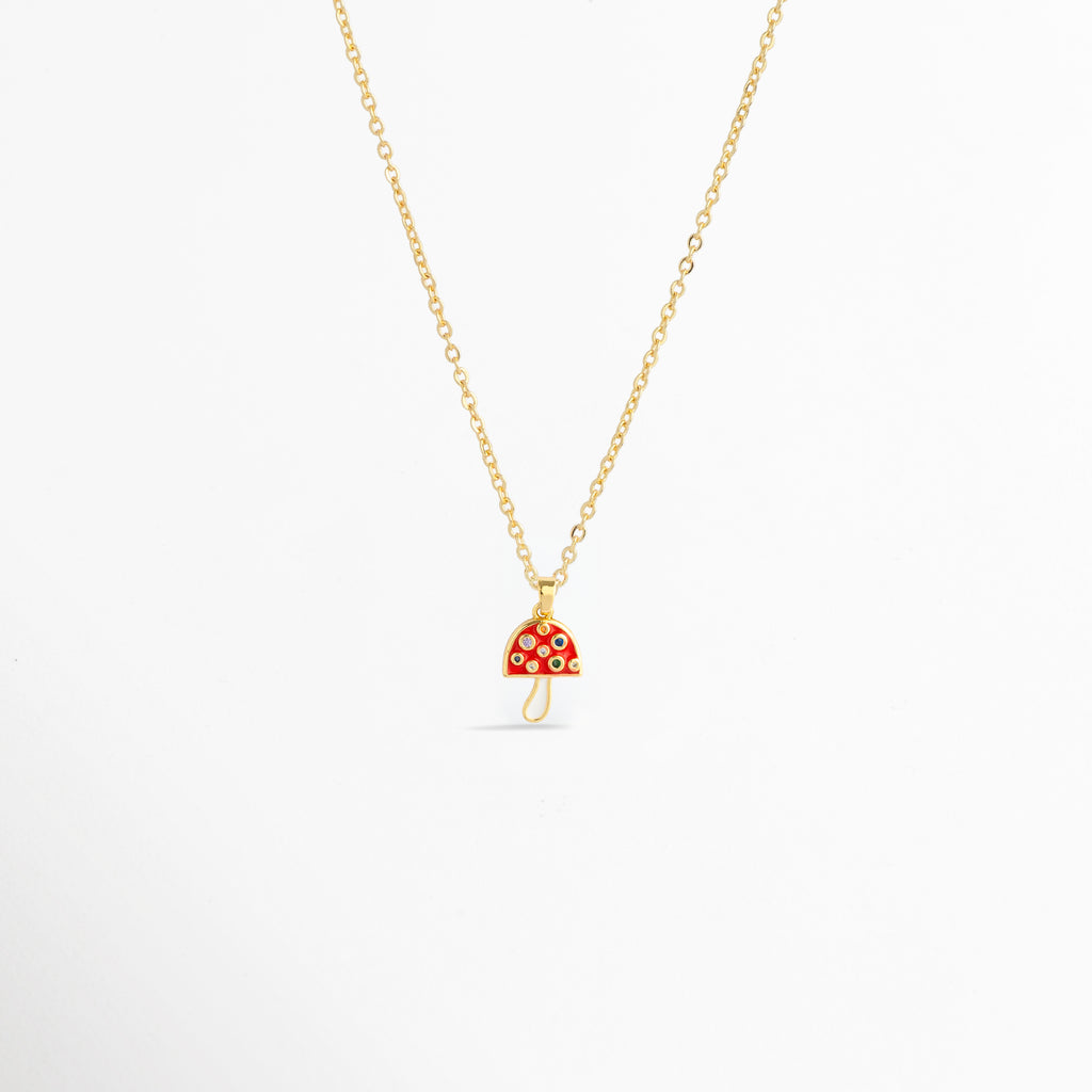 Charm Hongo Rojo montado como dije central en una fina cadena dorada sobre fondo blanco, Vista de collar con dije pequeño de hongo en esmalte rojo y pedrería multicolor de 2.1 cm enchapado en oro 18K, Perspectiva de gargantilla delicada con dije colgante en forma de seta roja y dorada con circonias, Muestra de escala del charm de hongo rojo incrustado con gemas en una cadena delgada enchapada en oro.