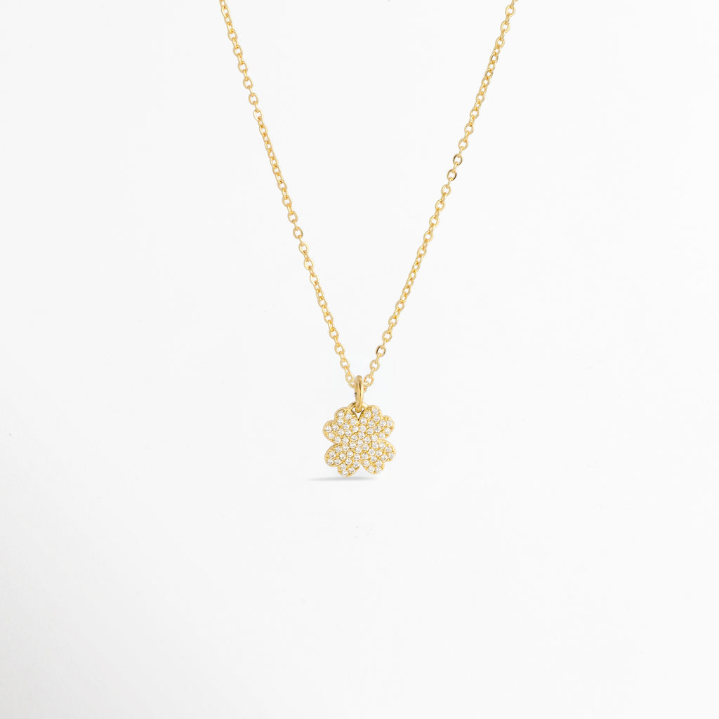 Charm Clover Spark montado como dije central en una fina cadena dorada sobre fondo blanco, Vista de collar con dije pequeño de trébol de cuatro hojas enchapado en oro con circonias brillantes de 1.8 cm, Perspectiva de gargantilla delicada con dije colgante en forma de trébol de la suerte dorado con pedrería, Muestra de escala del charm de trébol incrustado con circonias en una cadena delgada enchapada en oro.