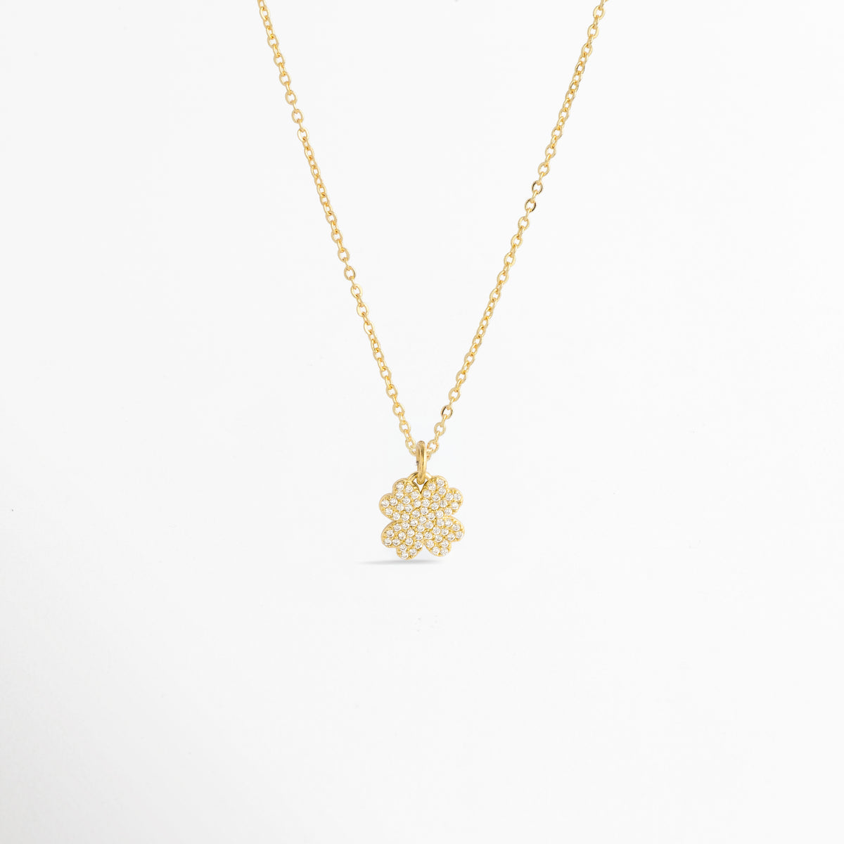 Charm Clover Spark montado como dije central en una fina cadena dorada sobre fondo blanco, Vista de collar con dije pequeño de trébol de cuatro hojas enchapado en oro con circonias brillantes de 1.8 cm, Perspectiva de gargantilla delicada con dije colgante en forma de trébol de la suerte dorado con pedrería, Muestra de escala del charm de trébol incrustado con circonias en una cadena delgada enchapada en oro.
