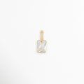 Charm Shimmer con gran circonia transparente de corte esmeralda y reasa vertical con micro-pavé, vista frontal sobre fondo blanco, Dije rectangular de 1.1 x 0.7 cm con cristal de circonia en engaste de bisel sobre metal dorado galvanizado, Vista de frente de dije charm de cobre dorado con gema baguette/esmeralda y asa decorada con pedrería, Charm de circonia transparente de corte rectangular con baño galvanizado brillante sobre superficie neutra.