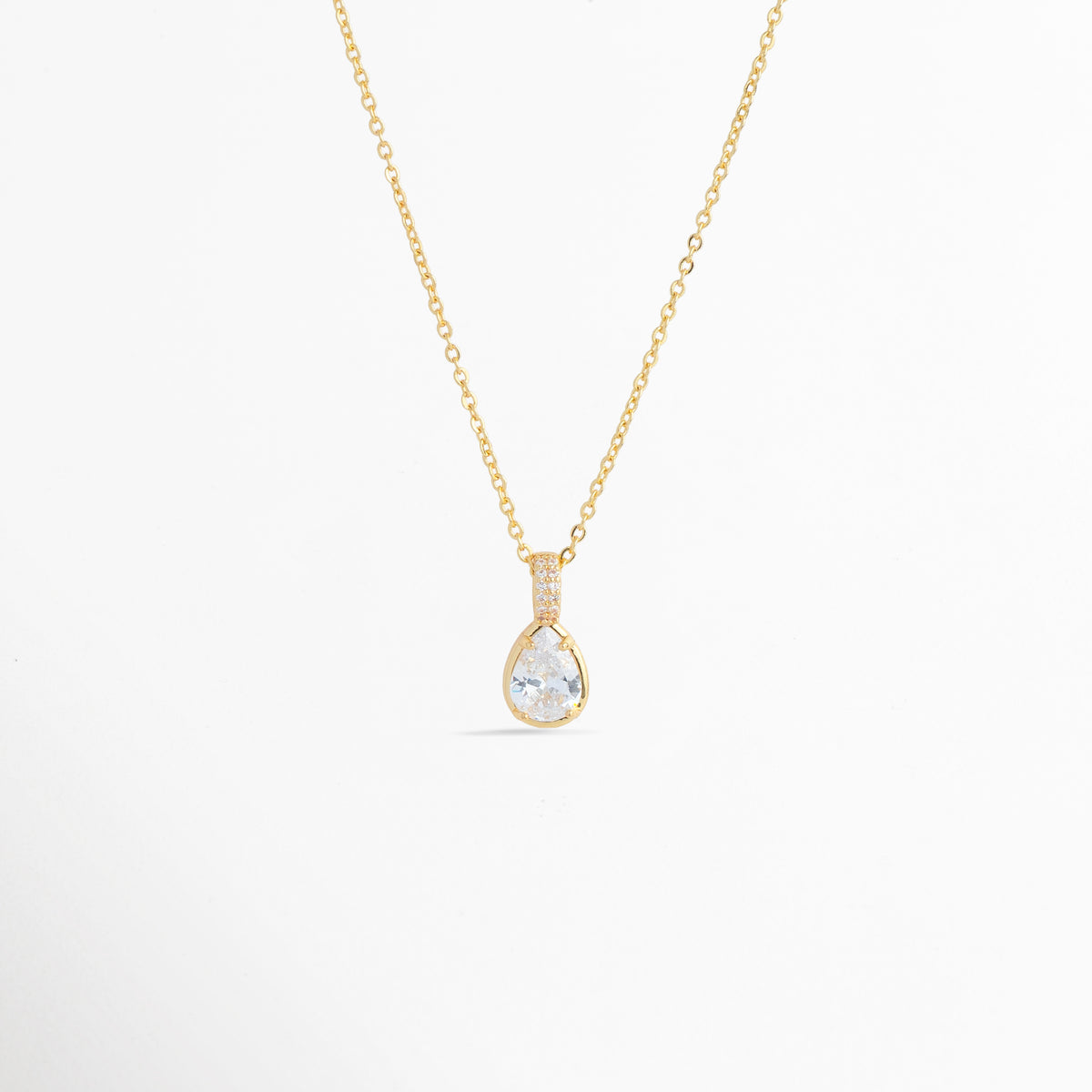 Charm Glow colocado como dije colgante en forma de gota en una delicada cadena dorada, vista frontal en plano general, Collar dorado sofisticado con dije en forma de lágrima de circonia transparente de inspiración romántica, Vista de colgante en forma de gota de luz sobre cadena fina enchapada sobre fondo blanco, Ejemplo de estilismo del Charm Glow usado como dije central para gargantilla o collar elegante.