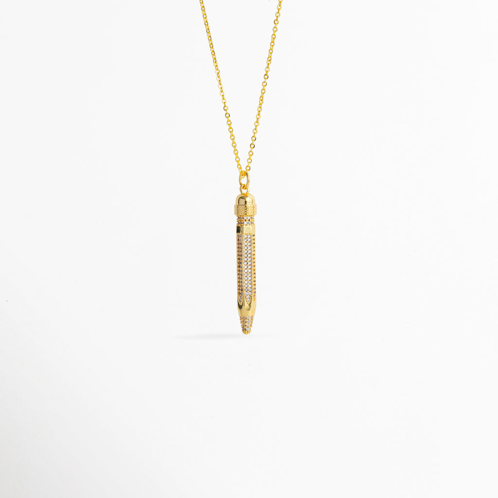 Charm Lápiz de cobre enchapado en oro de 4.2 cm de largo con cuerpo cuajado en pavé de circonias transparentes, vista frontal sobre fondo blanco, Vista de frente de dije estilizado en forma de lápiz dorado con incrustaciones de pedrería brillante suspendido de una fina cadena, Plano general de charm tridimensional en forma de lápiz enchapado en oro con detalles de circonias cristalinas sobre fondo neutro, Charm Lápiz destacando la punta dorada pulida y el resplandor