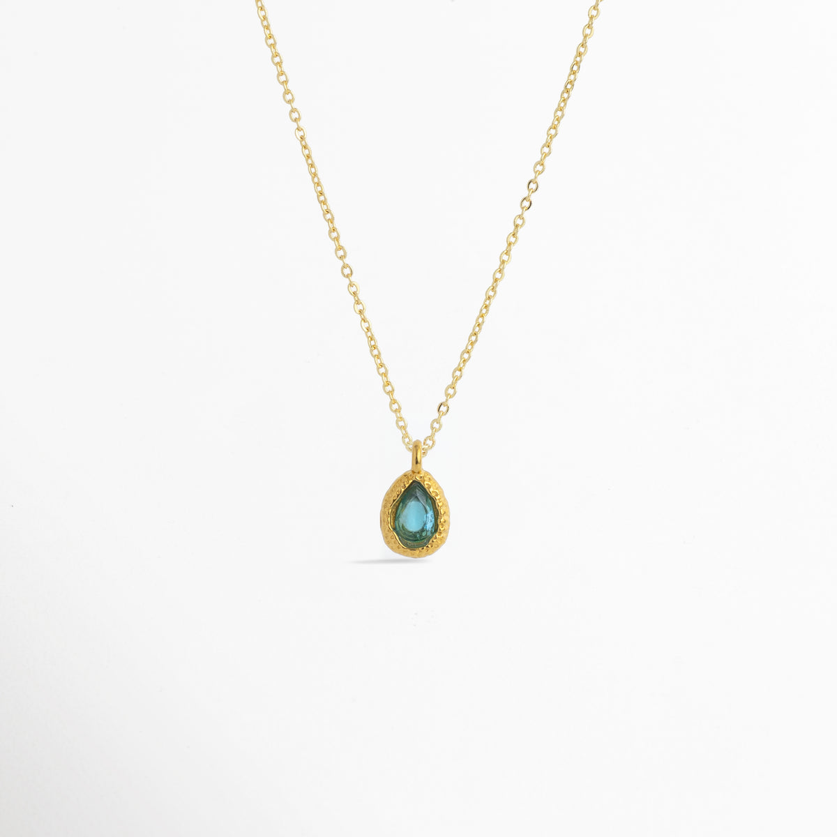 Charm Gota Azul Claro luciendo como colgante central en una fina cadena dorada, vista frontal en plano general, Collar dorado con dije en forma de gota azul claro de diseño sereno y elegante, Vista de colgante en tono azul mar sobre cadena fina enchapada en oro sobre fondo blanco, Ejemplo de estilismo del Charm Gota Azul Claro integrado como punto de color fresco en un collar dorado.