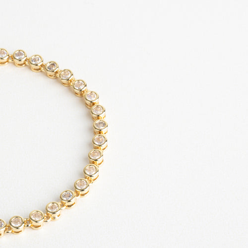 Zirconias cúbicas montadas con precisión sobre la base dorada, Acabado pulido con reflejos cálidos y brillantes, Detalle del engaste fino de cada piedra, Contraste entre el dorado y el brillo claro de las zirconias, Estructura delicada con incrustaciones alineadas