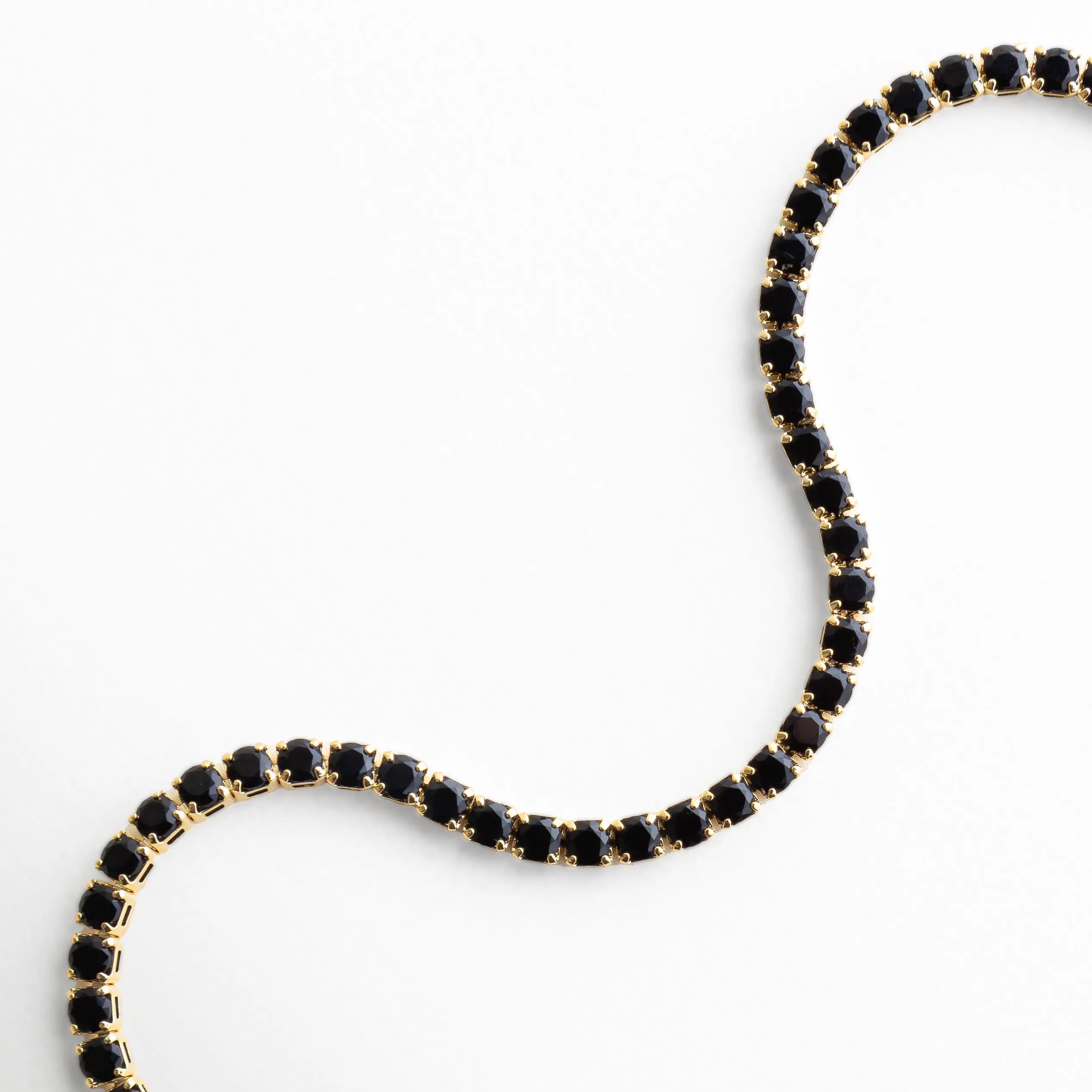 Pulsera flexible con zirconias negras y baño en oro blanco 18K, diseño elegante, Detalle de pulsera tipo tenis con piedras negras, acabado brillante sofisticado, Pulsera de cobre con zirconias negras en forma curva, estilo moderno femenino, Pulsera minimalista flexible con incrustaciones oscuras y acabado en oro blanco, Pulsera elegante con diseño ondulado y zirconias negras brillantes