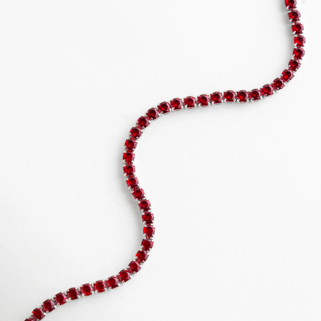 Pulsera de cristales rojos dispuestos en una línea continua, reflejando luz con cada movimiento.