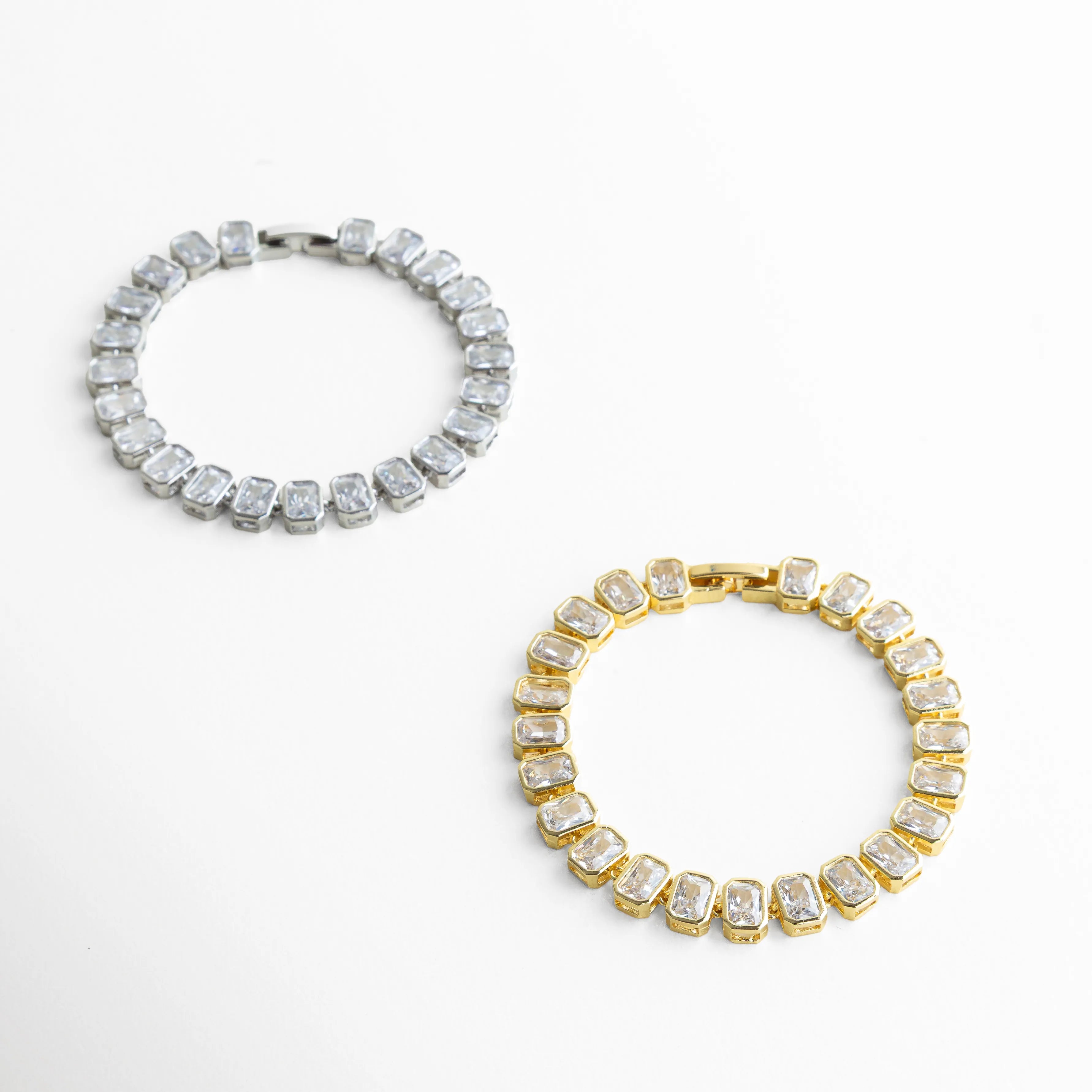 Pulsera Jung en versión dorada y plateada con zirconias brillantes, Comparación de pulseras tipo tenis en oro 18K y oro blanco, Dos pulseras elegantes con zirconias en acabado dorado y plateado, Pulsera tipo tenis en diferentes tonos con diseño sofisticado, Vista comparativa de pulseras brillantes dorada y plateada