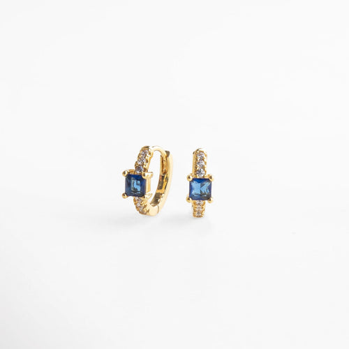 Primer plano de textura y piedras preciosas en aretes hoops dorados, combinación de zirconias y zafiro artificial, pieza que fusiona elegancia clásica con modernidad