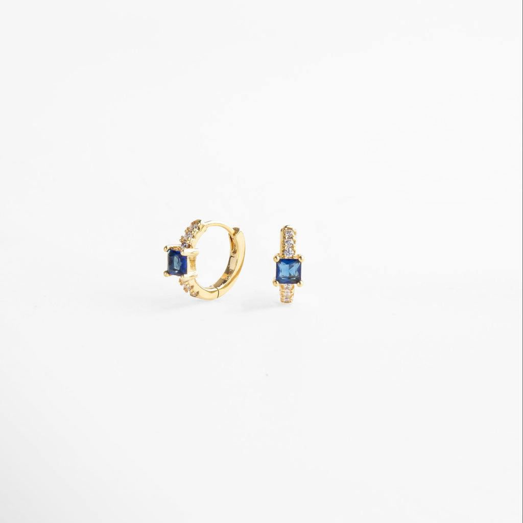 Detalle de aretes hoops con incrustaciones de zirconias que reflejan la luz, piedra color zafiro en el centro, diseño delicado y lujoso que aporta un toque de color intenso y brillo sutil