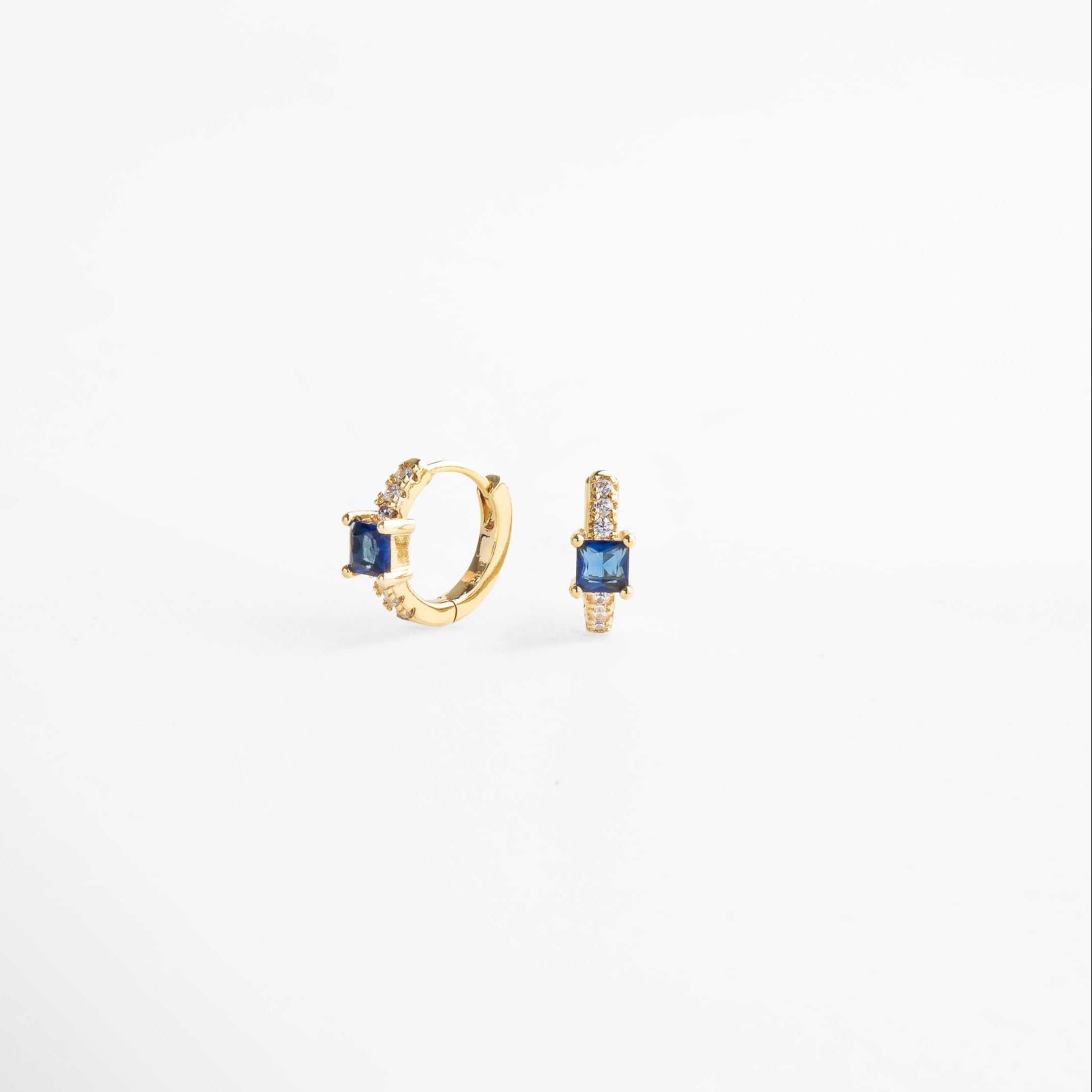 Detalle de aretes hoops con incrustaciones de zirconias que reflejan la luz, piedra color zafiro en el centro, diseño delicado y lujoso que aporta un toque de color intenso y brillo sutil