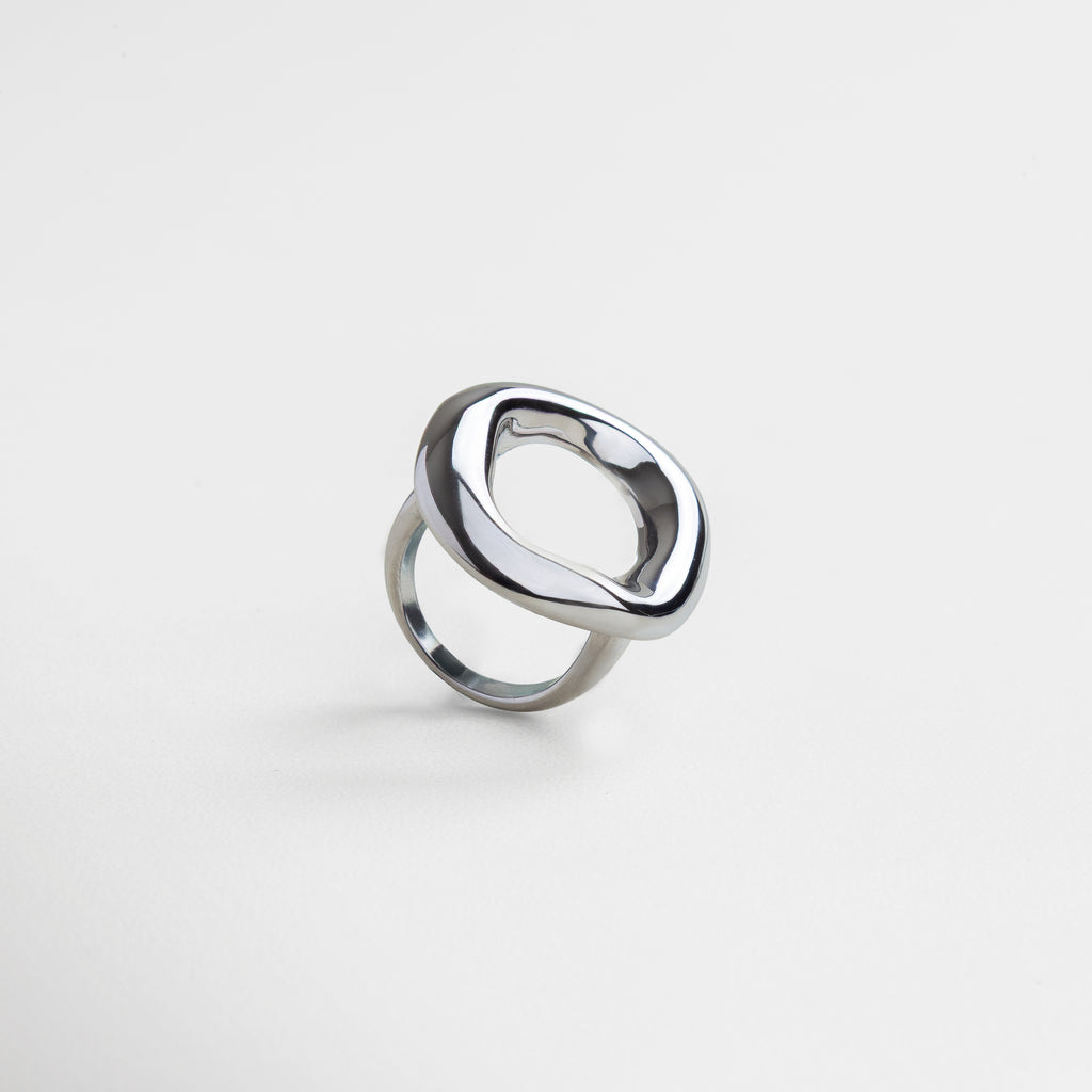 Anillo plateado con diseño curvo visto de perfil, Silueta ancha y elegante del Anillo Donna en ángulo, Joya contemporánea en acero inoxidable vista en diagonal, Diseño bold del anillo en perspectiva lateral