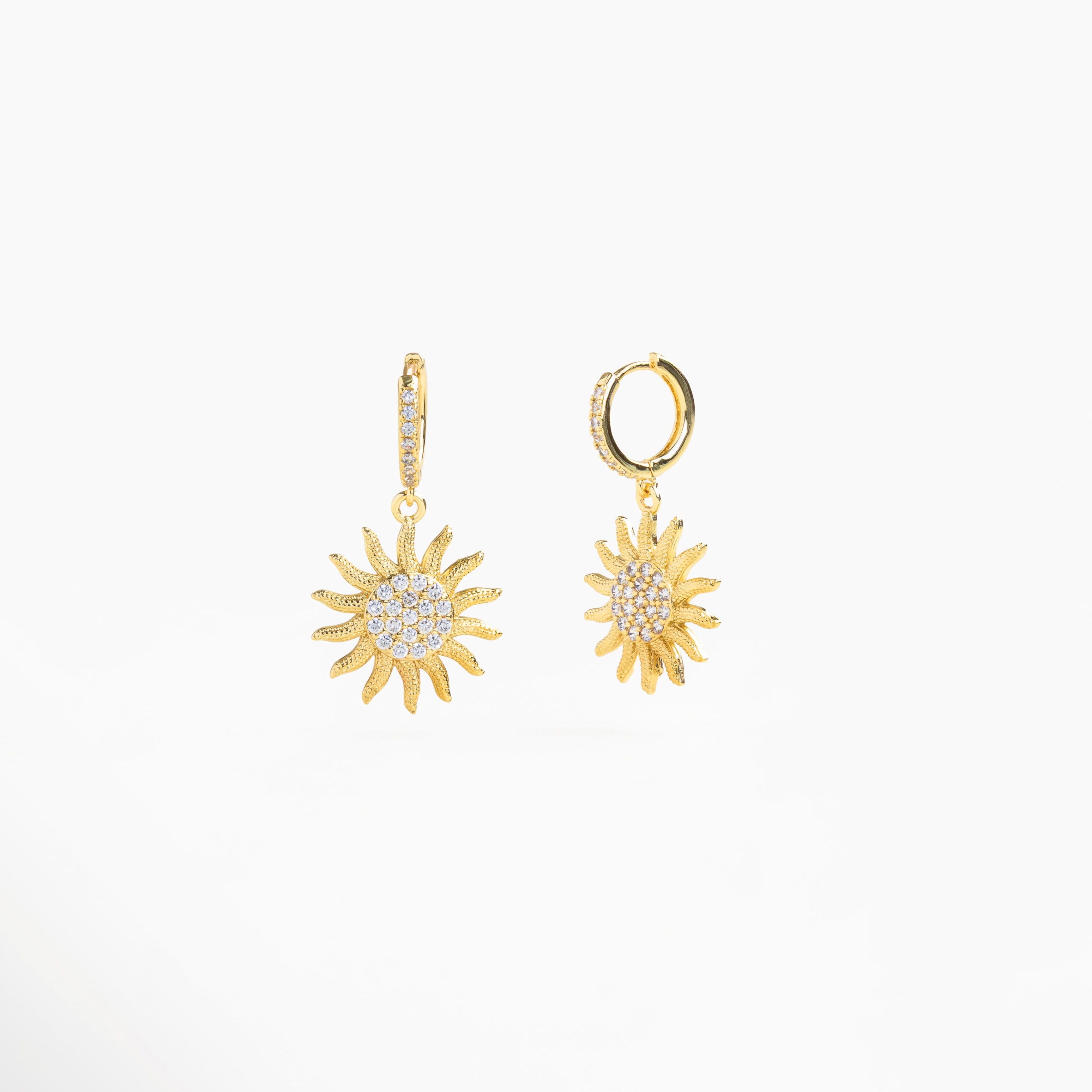 Aretes dorados largos puestos con zirconias relucientes, Cómo lucen los aretes sunrise en un look femenino, Pendientes de oro 18k en oreja con detalle colgante, Estilo elegante con aretes dorados y piedras, Inspiración de look con aretes colgantes dorados