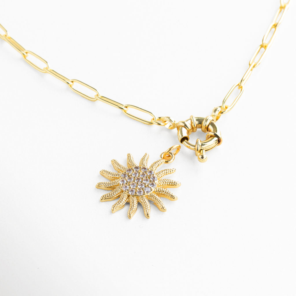 Detalle de zirconias en dije de sol dorado, Incrustaciones brillantes en collar con diseño solar, Acabado pulido y textura radiante del colgante, Primer plano del dije en forma de sol con piedras