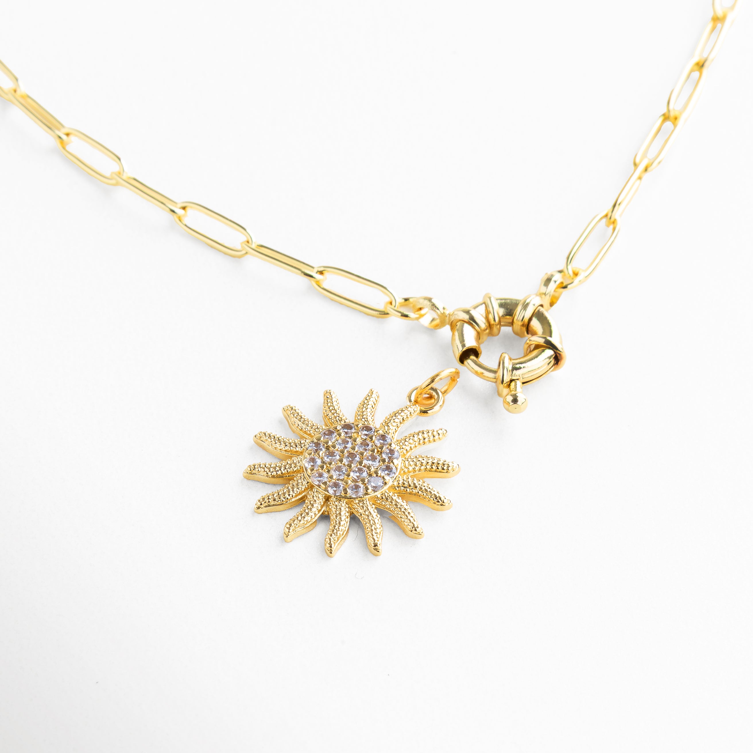 Detalle de zirconias en dije de sol dorado, Incrustaciones brillantes en collar con diseño solar, Acabado pulido y textura radiante del colgante, Primer plano del dije en forma de sol con piedras