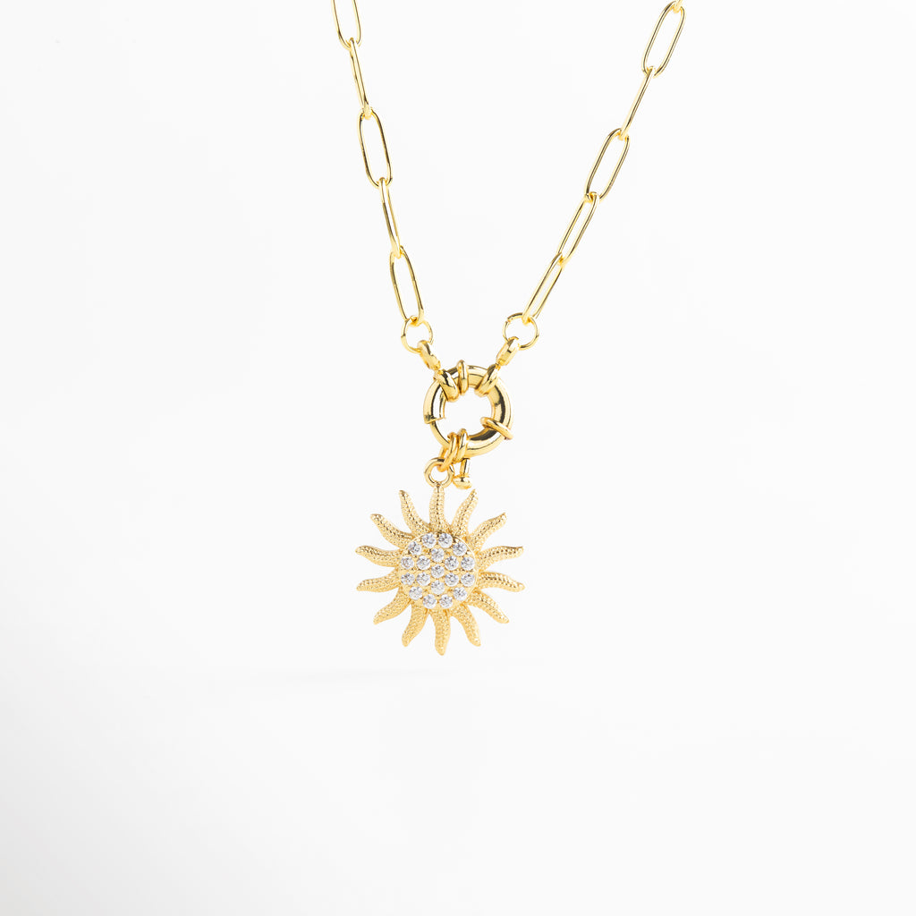 Colgante de sol visto en ángulo en collar dorado, Relieve del dije solar con zirconias en perspectiva, Vista angular que resalta la forma y brillo del sol, Collar dorado con colgante curvo y brillante