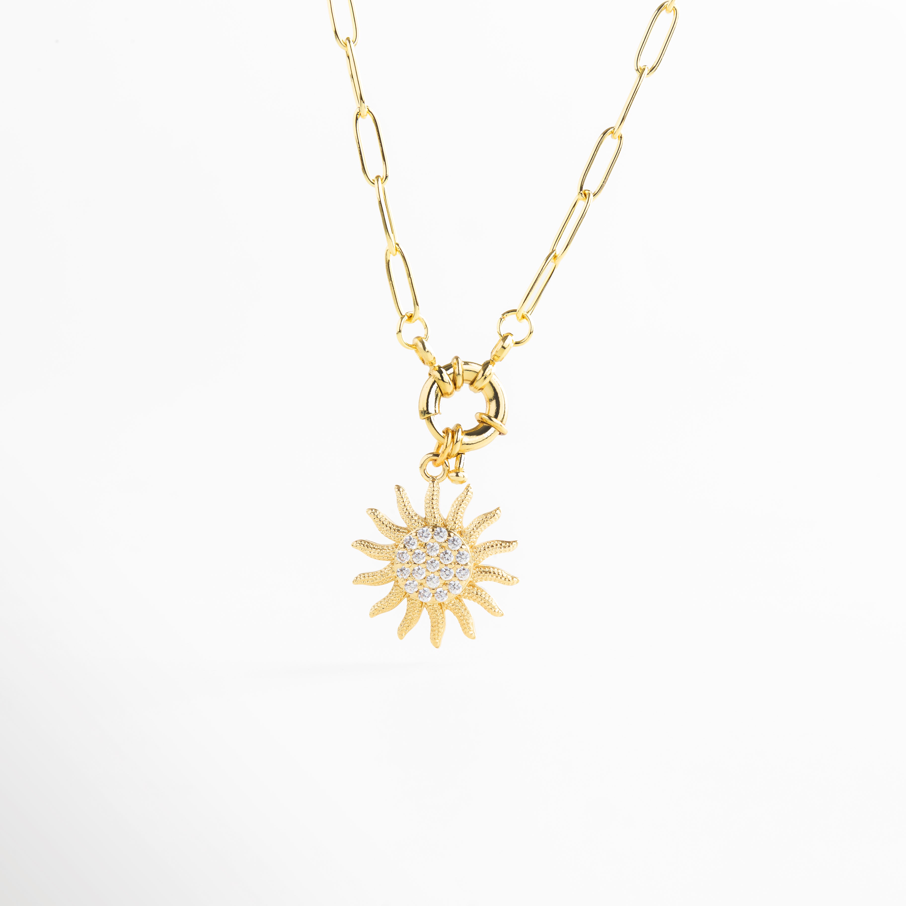 Colgante de sol visto en ángulo en collar dorado, Relieve del dije solar con zirconias en perspectiva, Vista angular que resalta la forma y brillo del sol, Collar dorado con colgante curvo y brillante