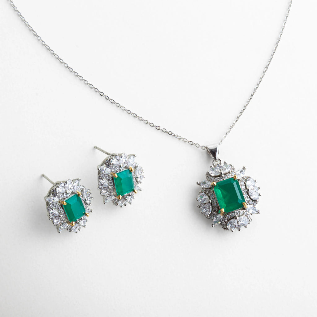 Set plateado compuesto por collar y aretes con piedras verdes tipo esmeralda, ambos rodeados por un halo de zirconias que reflejan la luz con intensidad. Una combinación de colores vibrante y elegante, perfecta para eventos de noche o celebraciones especiales.