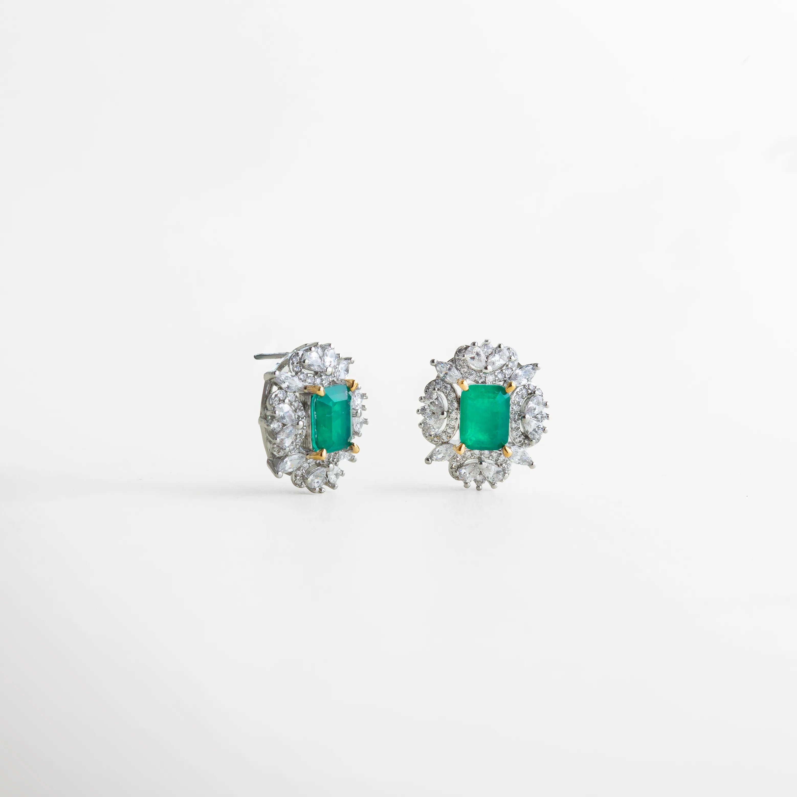 Vista lateral de los aretes con incrustaciones de zirconias y piedra verde central, destacando su volumen y estructura. La mezcla de tonos y cortes resalta la elegancia del diseño y la calidad del engaste, con una luz que recuerda a las joyas clásicas de alta gama.