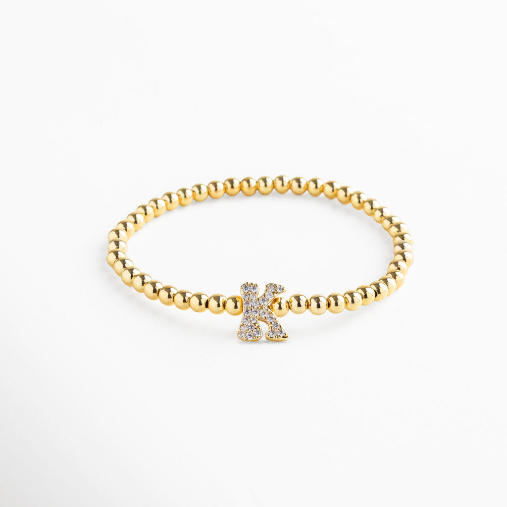 Pulsera elástica de cobre con recubrimiento enchapado en oro 18K e incrustaciones de zirconias, diseño de cuentas doradas con dije en forma de letra K personalizada, joya delicada y versátil de 1 x 0.7 cm ideal para uso diario.