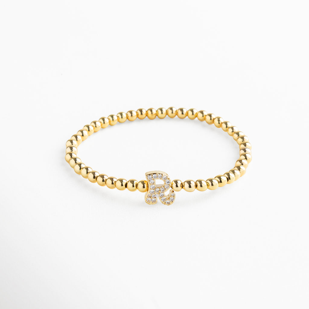 Pulsera elástica de cobre con recubrimiento enchapado en oro 18K e incrustaciones de zirconias, diseño de cuentas doradas con dije en forma de letra R personalizada, joya delicada y versátil de 1 x 0.7 cm ideal para uso diario.