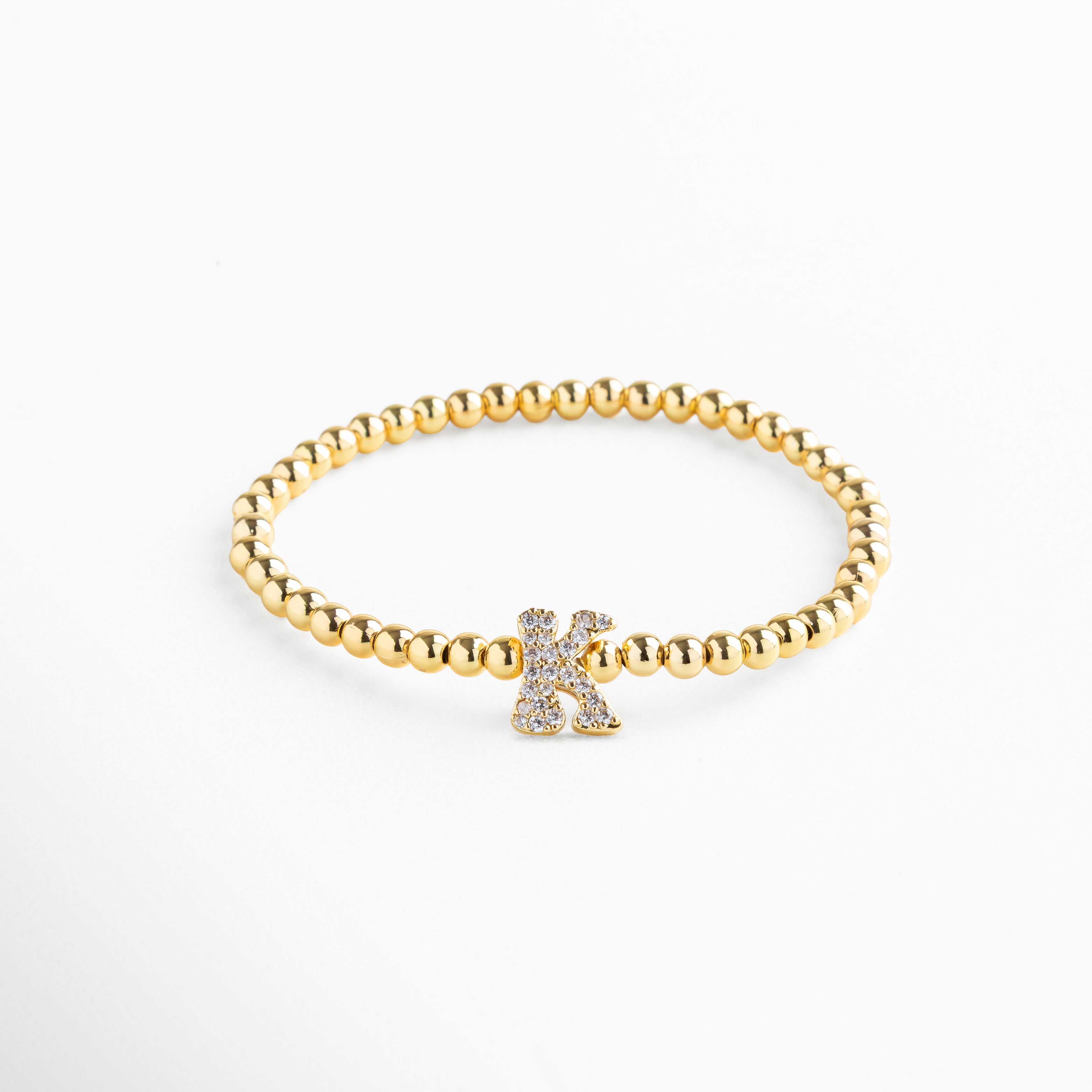 Pulsera elástica de cobre con recubrimiento enchapado en oro 18K e incrustaciones de zirconias, diseño de cuentas doradas con dije en forma de letra K personalizada, joya delicada y versátil de 1 x 0.7 cm ideal para uso diario.