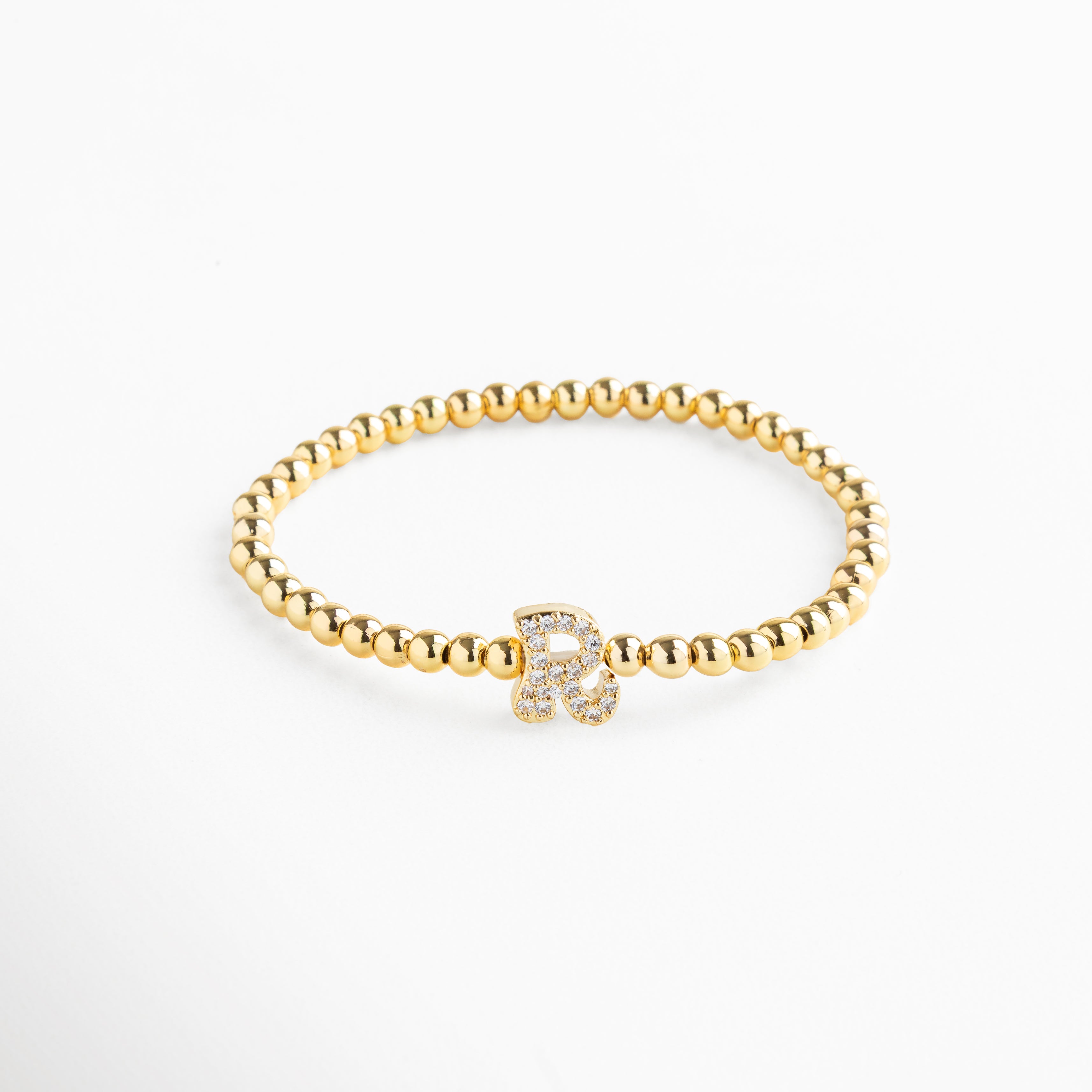 Pulsera elástica de cobre con recubrimiento enchapado en oro 18K e incrustaciones de zirconias, diseño de cuentas doradas con dije en forma de letra R personalizada, joya delicada y versátil de 1 x 0.7 cm ideal para uso diario.