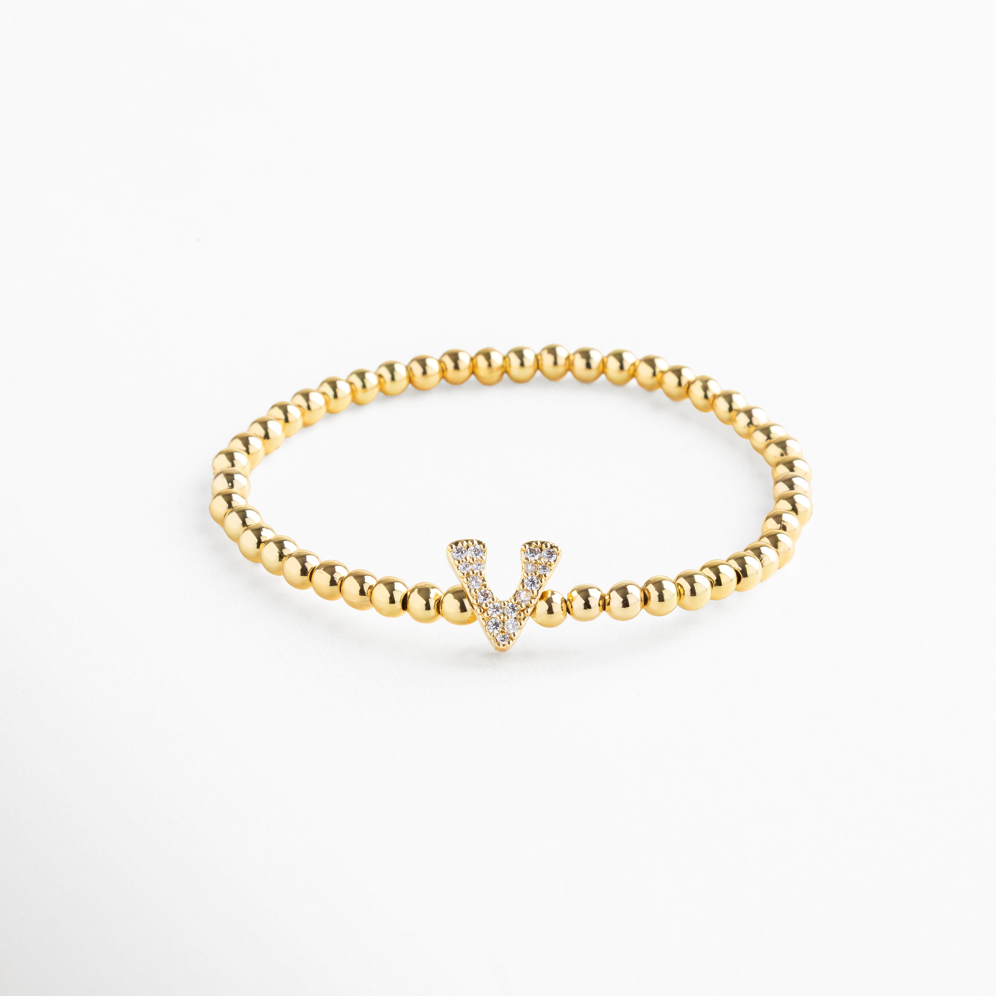 Pulsera elástica de cobre con recubrimiento enchapado en oro 18K e incrustaciones de zirconias, diseño de cuentas doradas con dije en forma de letra V personalizada, joya delicada y versátil de 1 x 0.7 cm ideal para uso diario.