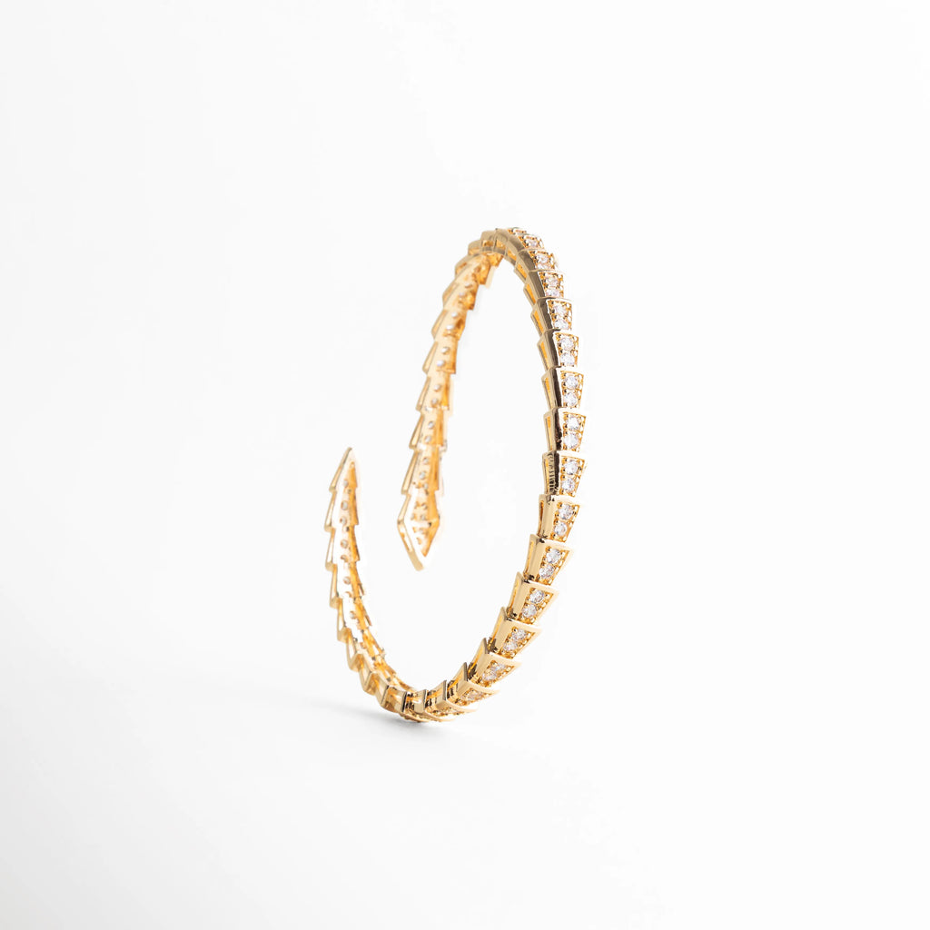 Vista superior del brazalete rígido ajustable mostrando su forma circular ergonómica, Pulsera de cobre con chapa de oro 18K y diseño de eslabones tipo escama, Brazalete abierto dorado que muestra la flexibilidad y el diseño continuo de circonias, Pulsera minimalista pero audaz con estructura dorada y piedras brillantes, Accesorio de muñeca ajustable de 12 cm a 17 cm en acabado oro y circonias.