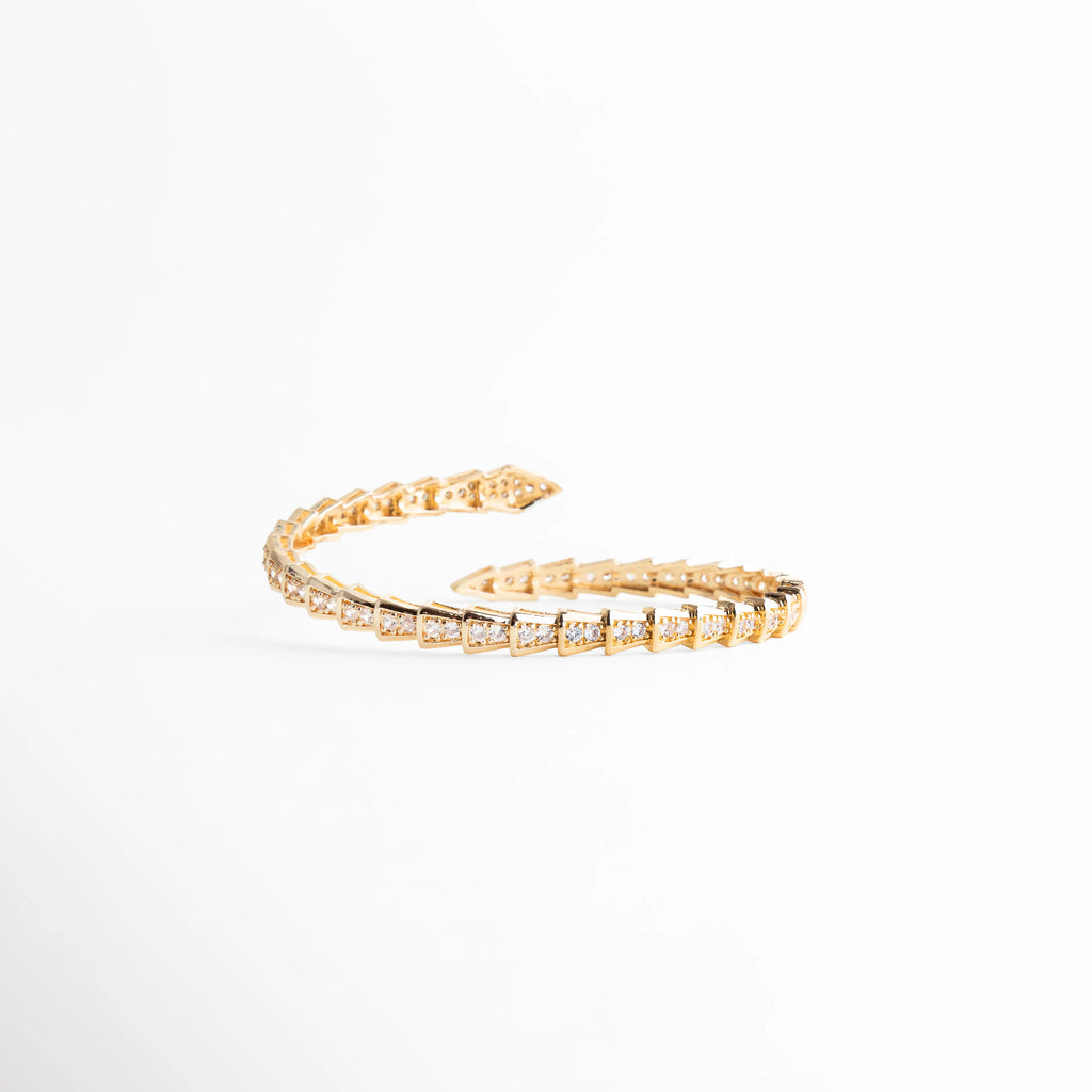 Detalle del diseño abierto ajustable del brazalete de oro y circonias cúbicas, Pulsera flexible de lujo accesible con base de cobre y recubrimiento de plata y oro, Vista de perfil que muestra el acabado pulido y la elegancia del brazalete, Brazalete ajustable para diferentes medidas de muñeca (12-17 cm) con brillo premium, Terminación detallada de las puntas con circonias en pulsera envolvente dorada.