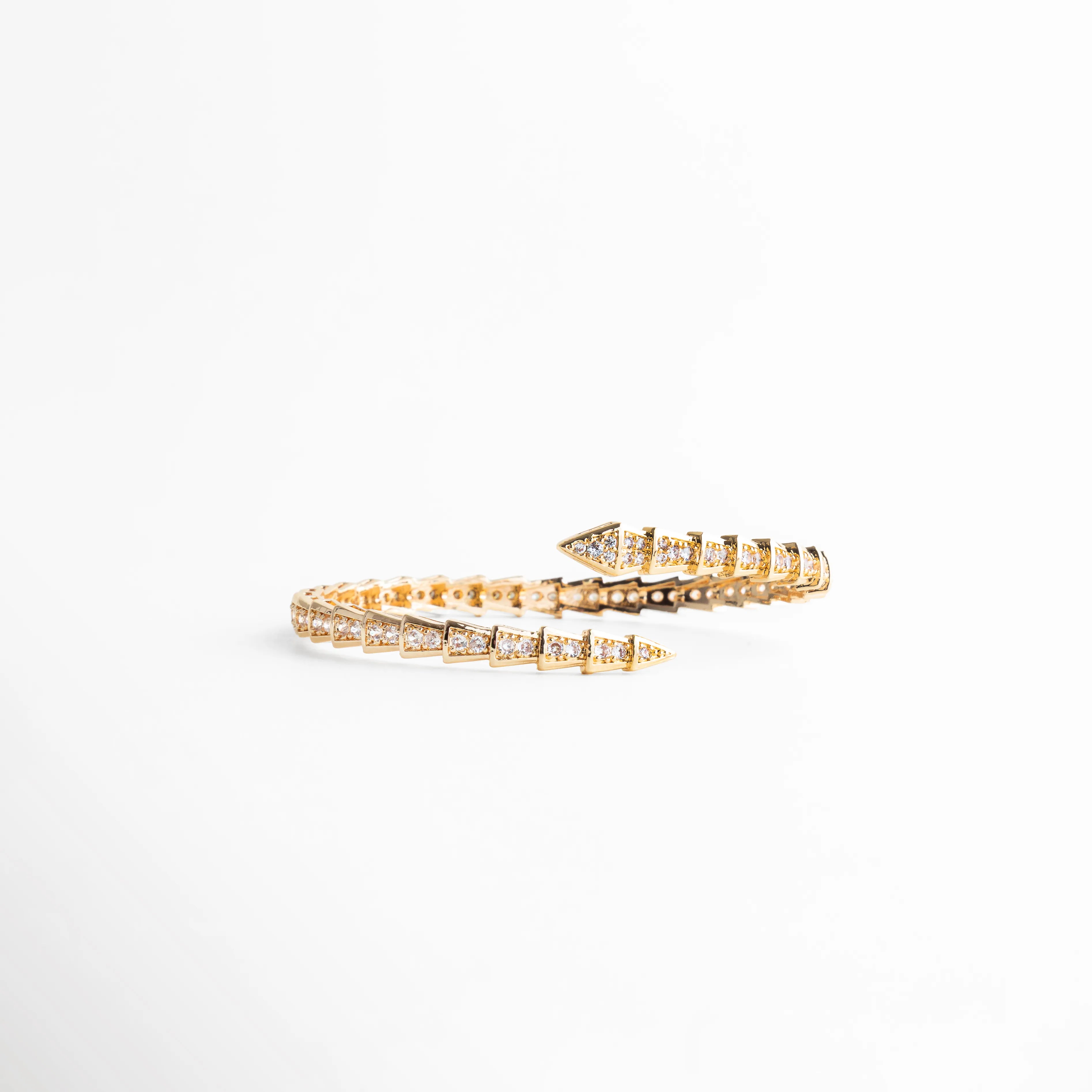 Brazalete ajustable de oro 18K con diseño de escamas y puntas triangulares con circonias, Pulsera rígida abierta tipo serpiente con baño de oro y cristales brillantes, Detalle de brazalete de lujo con incrustaciones de circonia cúbica y acabado en oro 18K, Joyería elegante: brazalete dorado con diseño geométrico de flechas y brillo intenso, Brazalete "wrap" de oro con detalles de circonias, ideal para un look de joyería de alta gama.