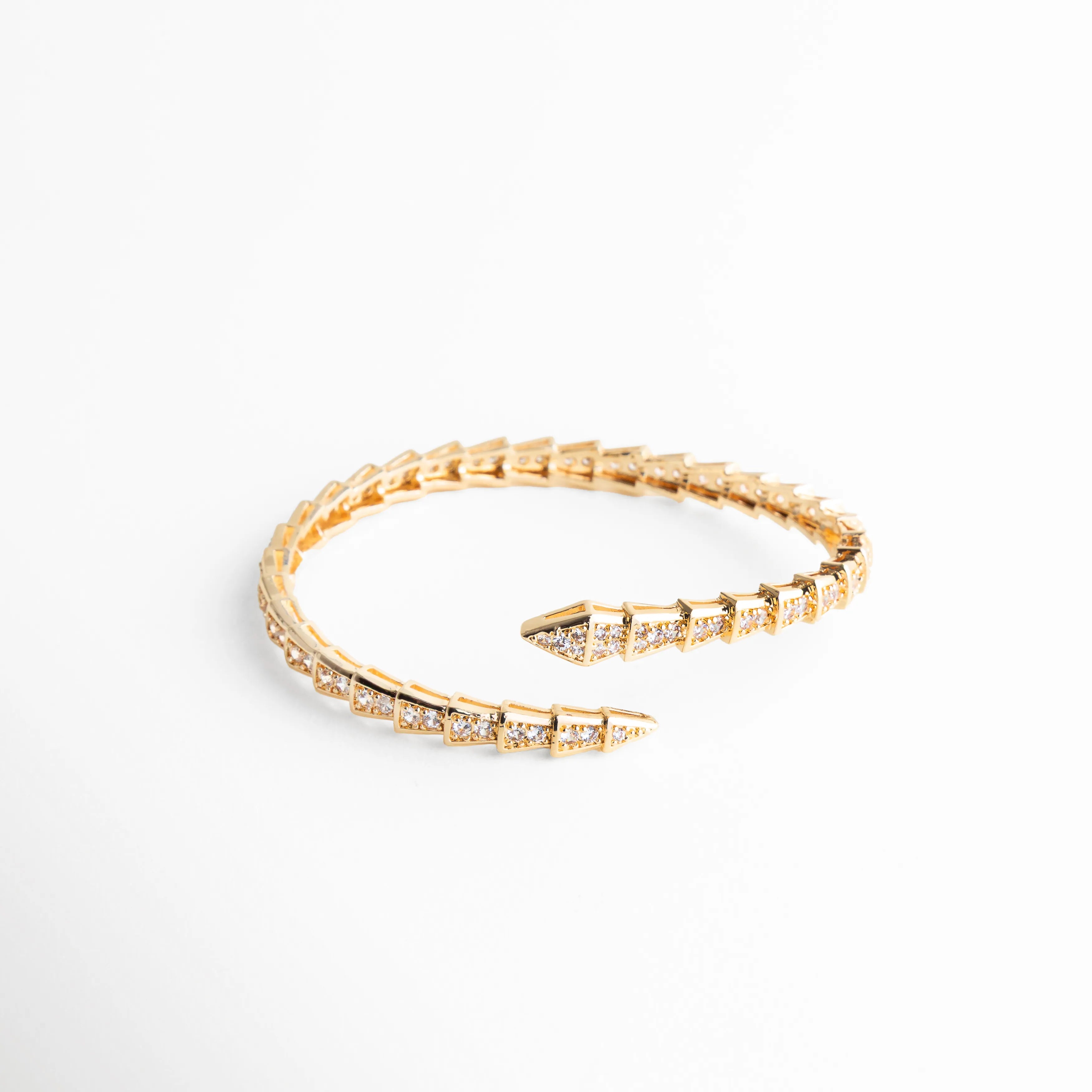 Perspectiva lateral de brazalete con textura de escamas doradas y micro-pavé de circonias, Brazalete de moda con relieve geométrico y baño de oro 18K sobre base de cobre, Detalle de la calidad del enchapado y el engaste de las piedras en el brazalete, Pulsera dorada ajustable con diseño de serpiente moderna y terminaciones en punta, Vista angular que resalta el brillo de las circonias cúbicas en la estructura dorada.