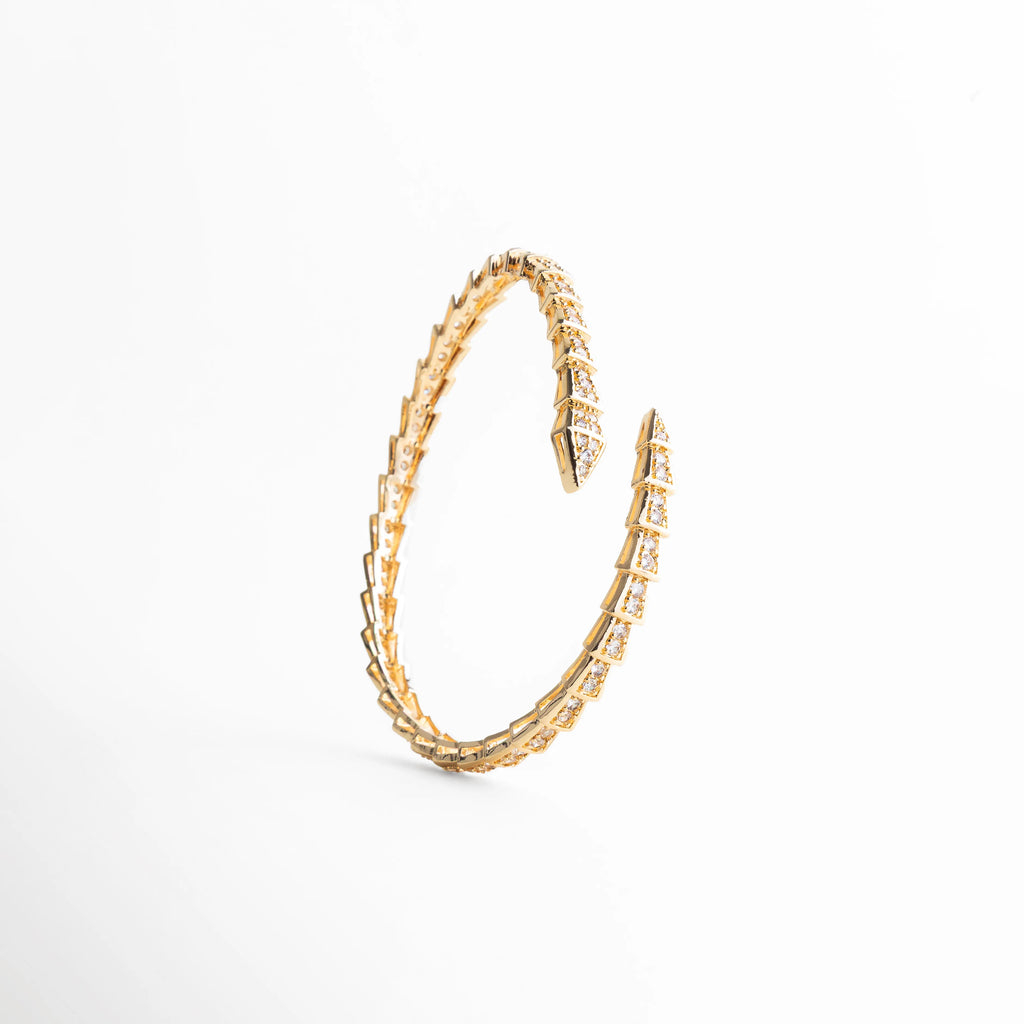 Vista de pájaro del brazalete de 1 cm de ancho con diseño de flecha doble, Brazalete envolvente dorado con patrón de escamas brillantes para mujer, Proporción y diseño del brazalete ajustable con acabado de lujo en oro 18K, Pulsera rígida de diseño arquitectónico con incrustaciones de cristales transparentes, Joyería contemporánea: brazalete ancho dorado con terminaciones cruzadas.