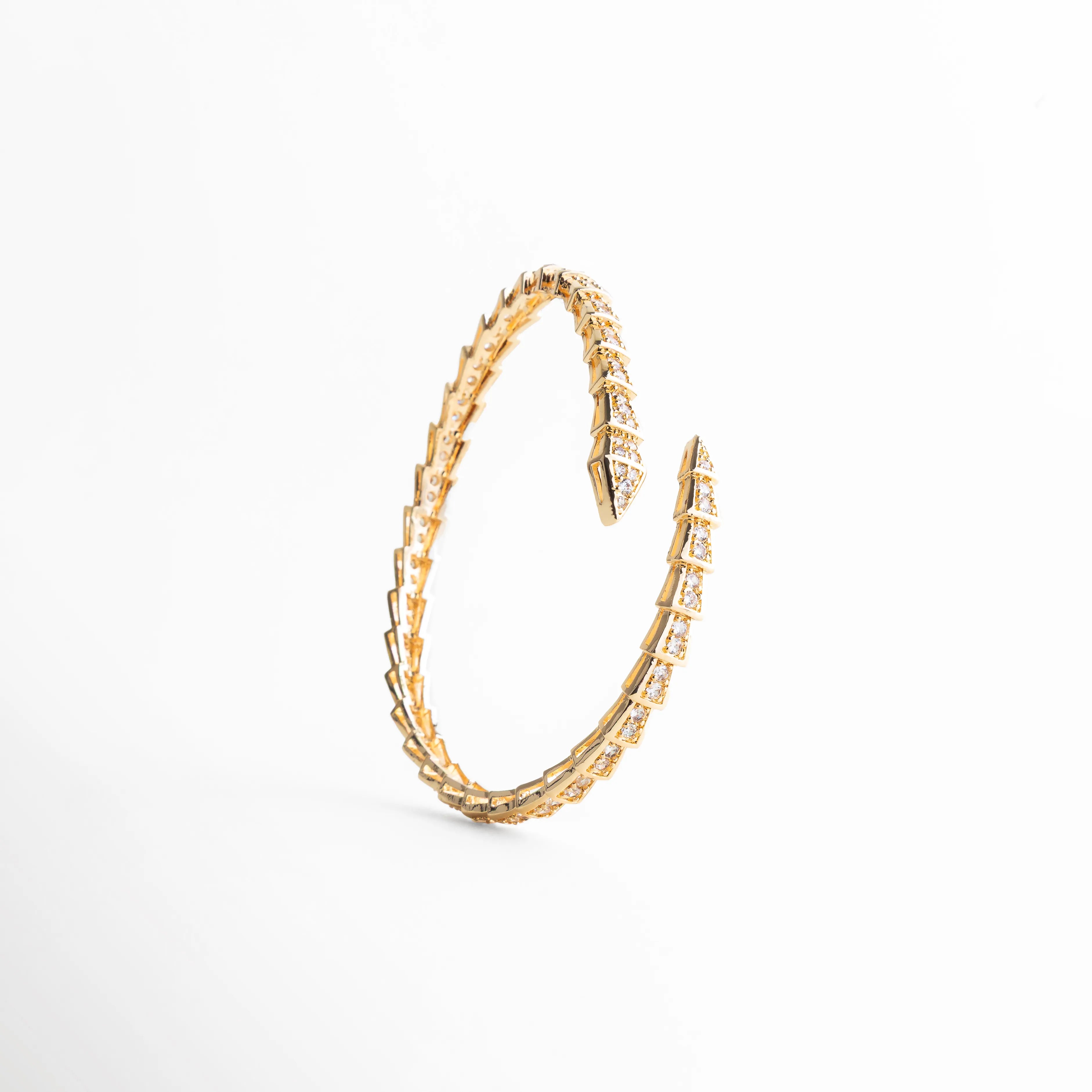 Vista de pájaro del brazalete de 1 cm de ancho con diseño de flecha doble, Brazalete envolvente dorado con patrón de escamas brillantes para mujer, Proporción y diseño del brazalete ajustable con acabado de lujo en oro 18K, Pulsera rígida de diseño arquitectónico con incrustaciones de cristales transparentes, Joyería contemporánea: brazalete ancho dorado con terminaciones cruzadas.