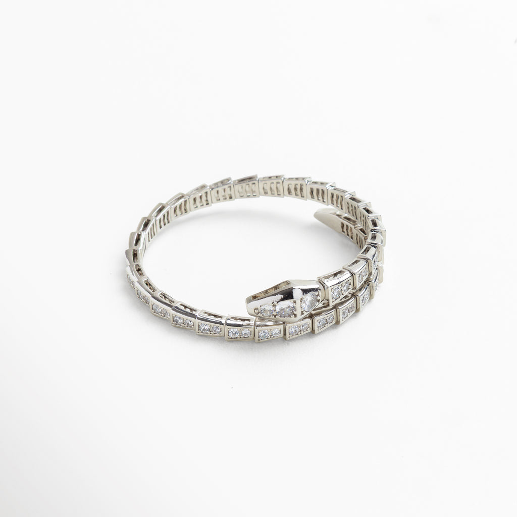 Primer plano de las incrustaciones de zirconias cúbicas que simulan escamas, Detalle del cierre con forma de cabeza de serpiente pulida, Textura articulada que aporta movimiento y flexibilidad, Acabado pulido en oro blanco con brillo metálico delicado, Detalle de los cristales brillantes en superficie reflectante