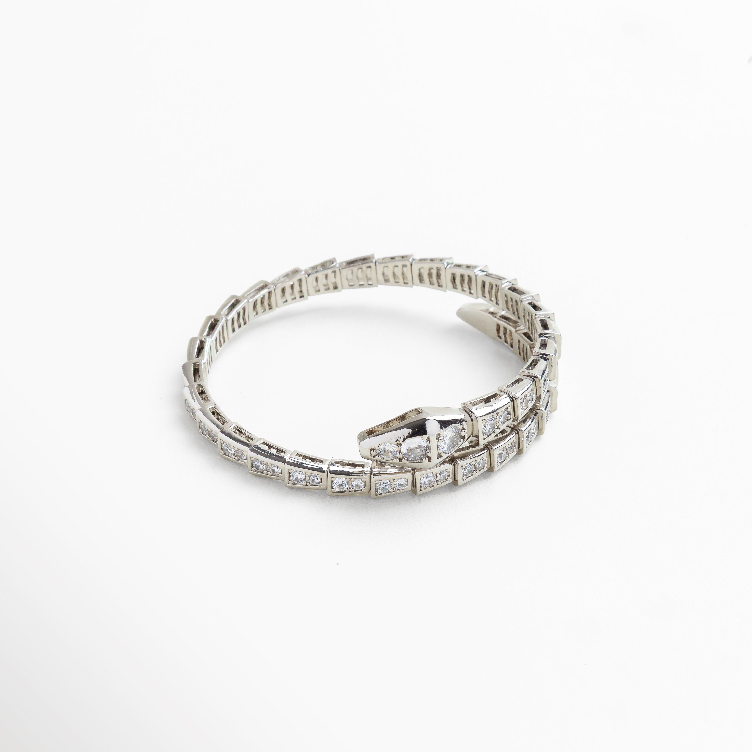 Primer plano de las incrustaciones de zirconias cúbicas que simulan escamas, Detalle del cierre con forma de cabeza de serpiente pulida, Textura articulada que aporta movimiento y flexibilidad, Acabado pulido en oro blanco con brillo metálico delicado, Detalle de los cristales brillantes en superficie reflectante