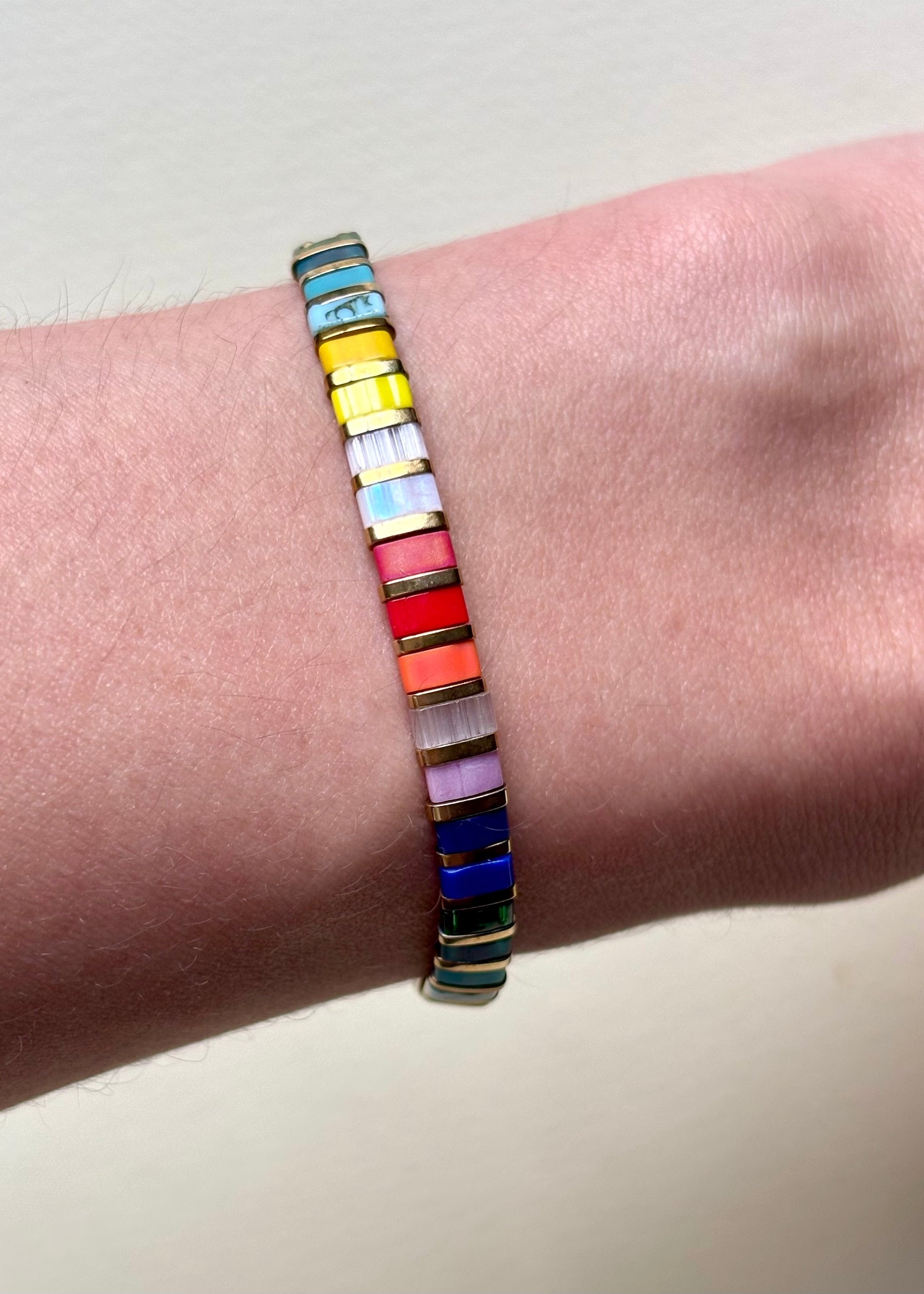 Vista de la Pulsera Rectángulos Colores puesta sobre la muñeca luciendo su perfil delgado y tono multicolor, Toma de estilo de vida mostrando la pulsera elástica de cuentas Miyuki Tila ajustada a la muñeca,  Muestra de la comodidad y ajuste flexible de la pulsera de rectángulos coloridos en uso diario, Plano medio de la pulsera elástica plana destacando su vibrante patrón de colores sobre la piel. 