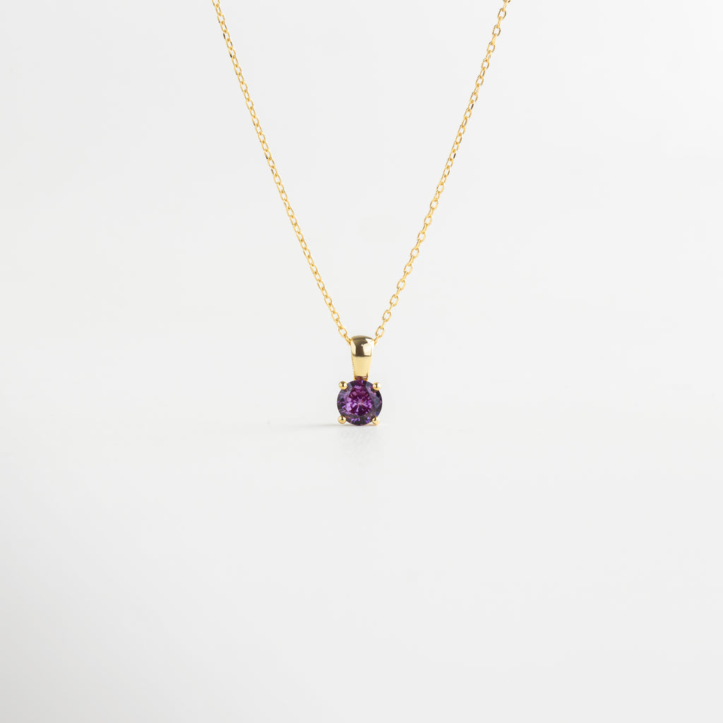 Vista superior del Collar del Mes extendido, mostrando su longitud de 22 cm y piedra central de color. Collar dorado con piedra pequeña de color visto desde arriba, resaltando su delicadeza y diseño sutil.
Toma cenital del collar elaborado en plata 925 con acabado dorado y zirconia central de 0.5 mm.
Collar del Mes extendido en plano superior, con cada versión luciendo una piedra distinta y colorida. Perspectiva desde arriba del Collar del Mes, con detalle central brillante y cadena dorada l
