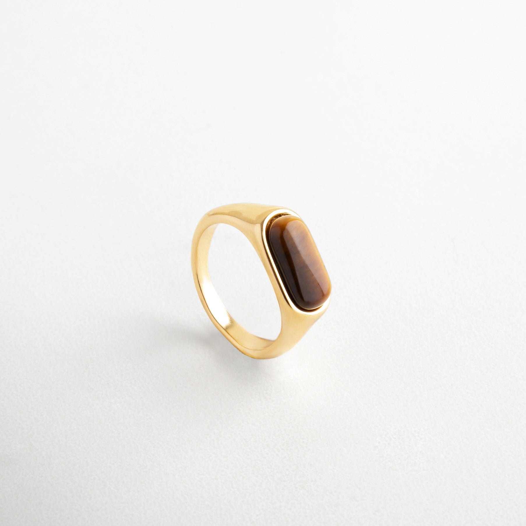 Anillo dorado con piedra ojo de tigre vista lateral, Perfil del anillo con diseño sofisticado y piedra natural, Anillo de acero inoxidable con reflejos cálidos, Diseño estructurado con piedra en tonos marrones y dorados