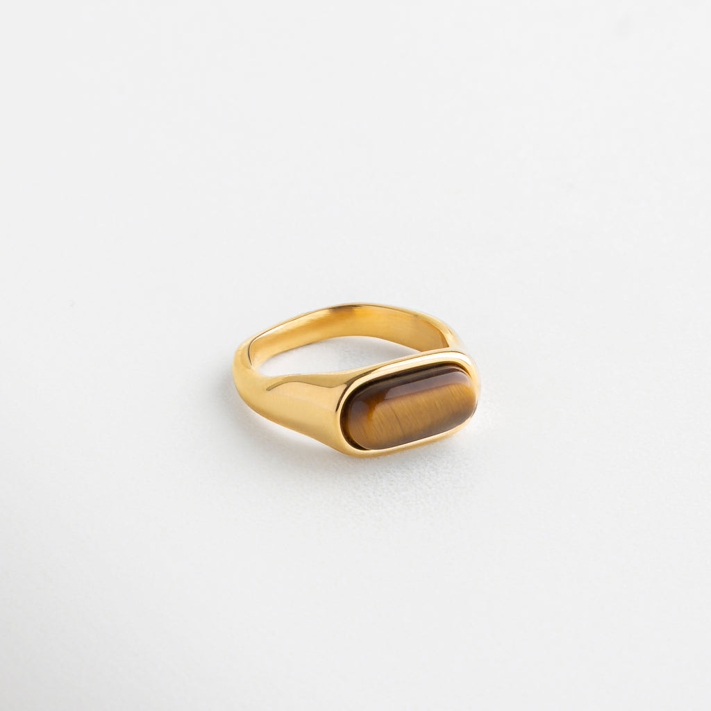 Detalle de anillo con piedra ojo de tigre pulida, Incrustación de piedra natural en anillo dorado, Textura de ojo de tigre en corte rectangular suave, Acabado dorado con piedra ojo de tigre facetada