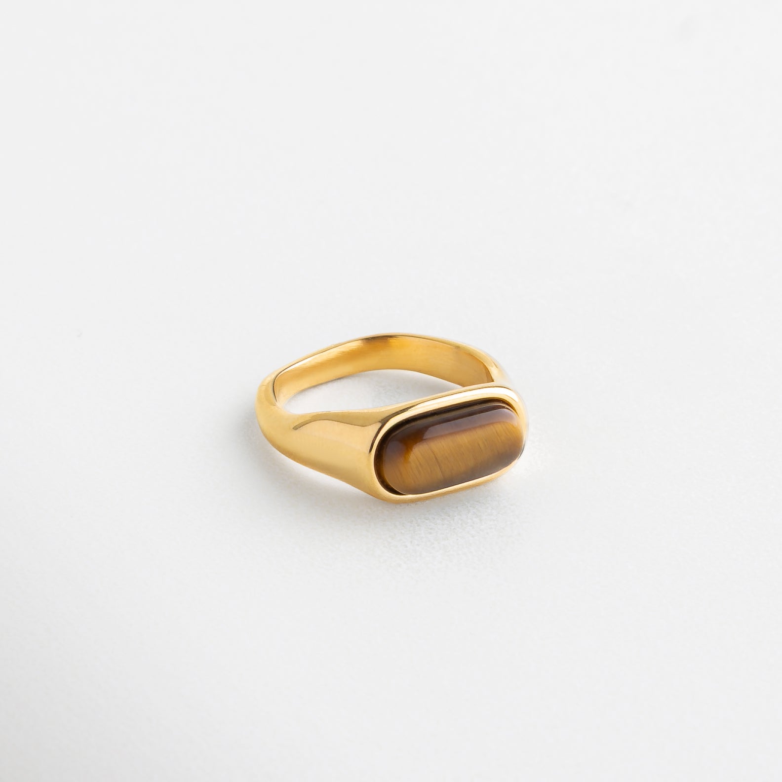 Detalle de anillo con piedra ojo de tigre pulida, Incrustación de piedra natural en anillo dorado, Textura de ojo de tigre en corte rectangular suave, Acabado dorado con piedra ojo de tigre facetada