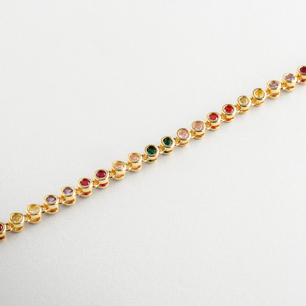 Pulsera Rodas Colores vista en ángulo con destellos vivos, Diseño en dorado con zirconias de diferentes colores, Pulsera estilizada con textura multicolor y dorado, Acentos vibrantes en pulsera con estructura delicada