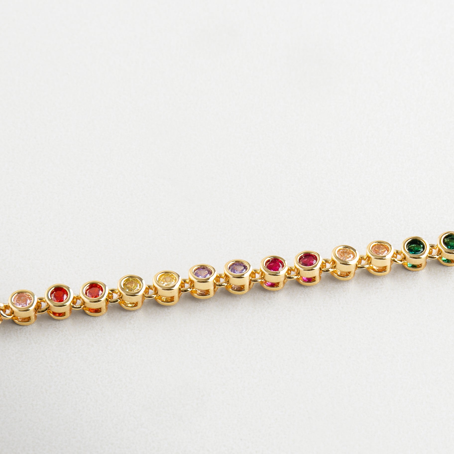 Detalle de zirconias cúbicas de colores en pulsera dorada, Primer plano de piedras multicolor sobre chapa de oro, Incrustaciones coloridas en pulsera con acabado brillante, Zirconias facetadas en gama multicolor sobre oro