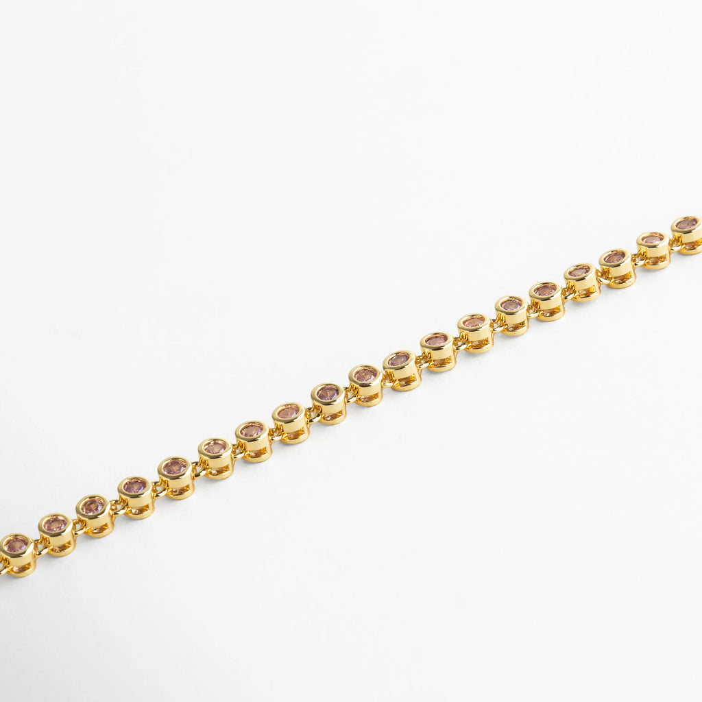 Pulsera dorada con cristales rosa empolvado engastados en estructura circular, aportando un brillo sutil y romántico.