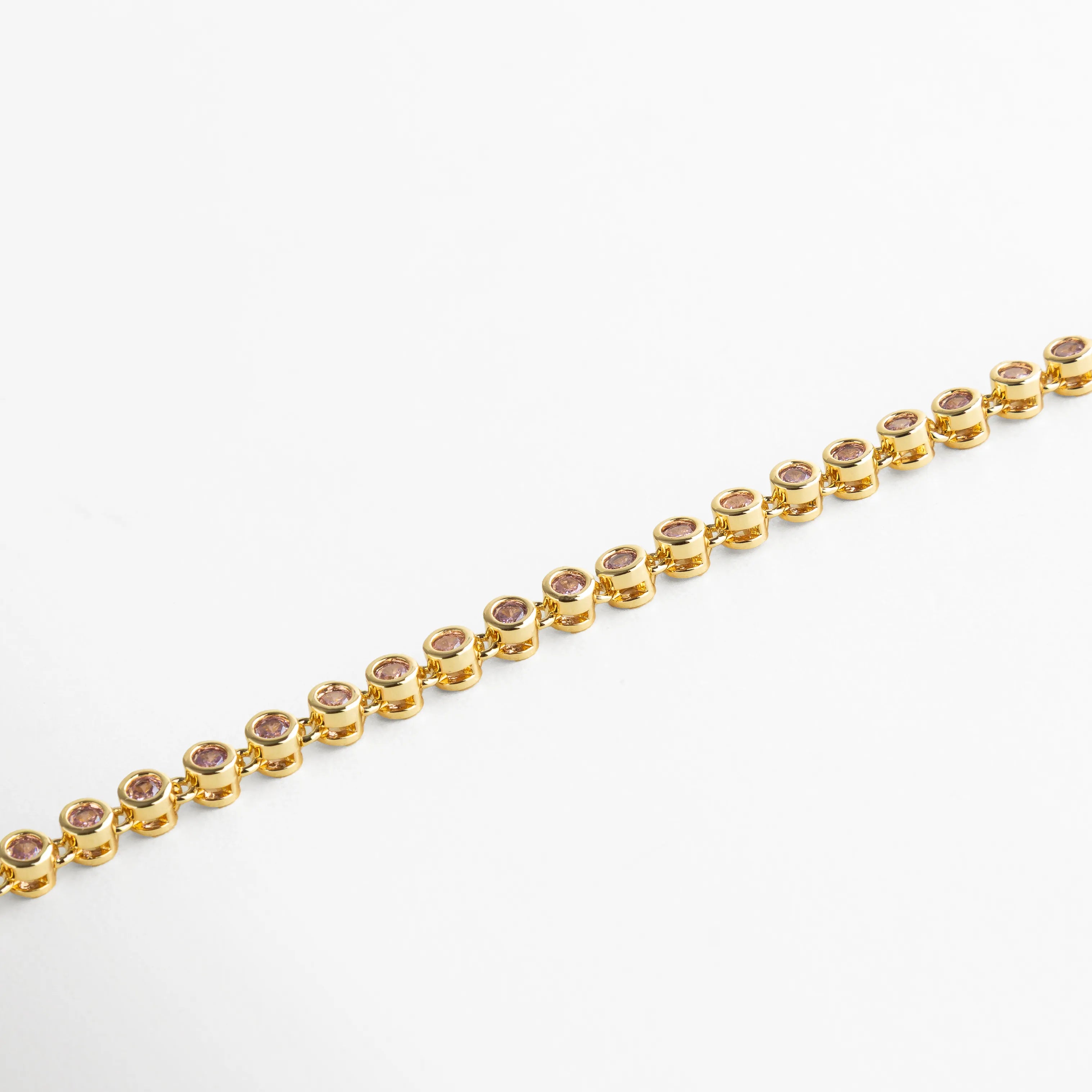 Pulsera dorada con cristales rosa empolvado engastados en estructura circular, aportando un brillo sutil y romántico.