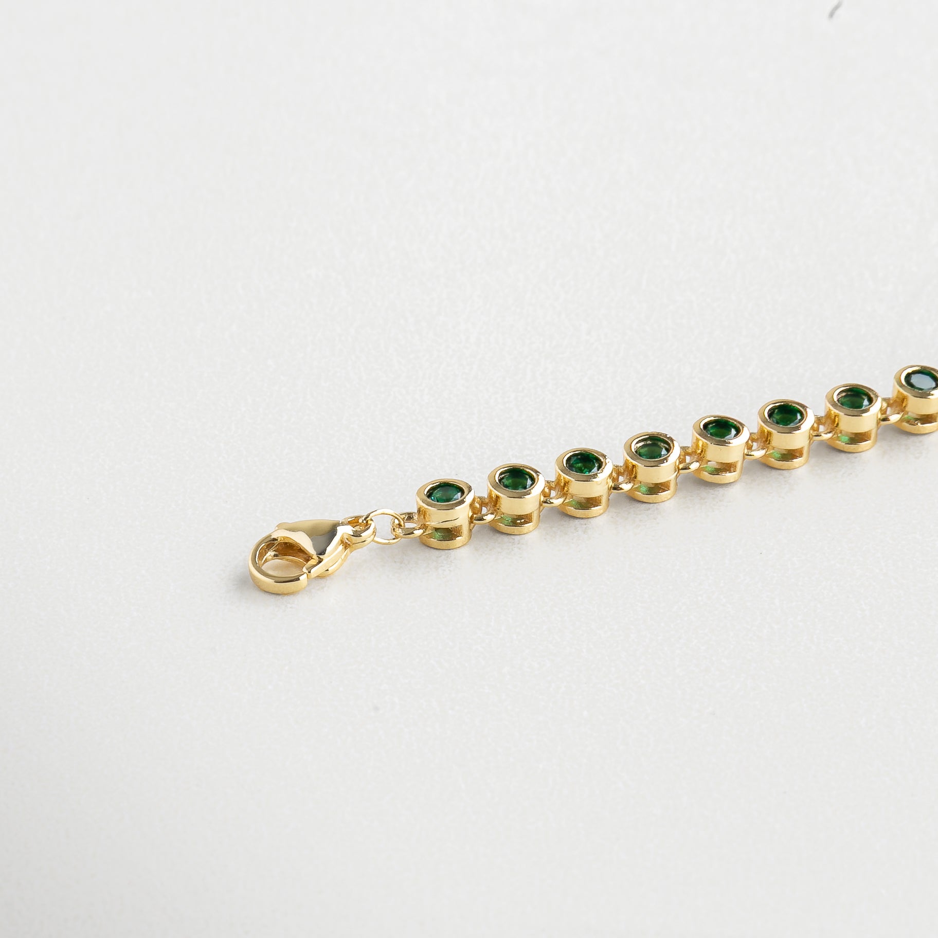 Pulsera Rodas Verde vista en ángulo con brillo sutil, Diseño de pulsera dorada con zirconias verdes facetadas, Pulsera dorada con efecto vibrante desde lateral, Estructura delicada con acentos verdes